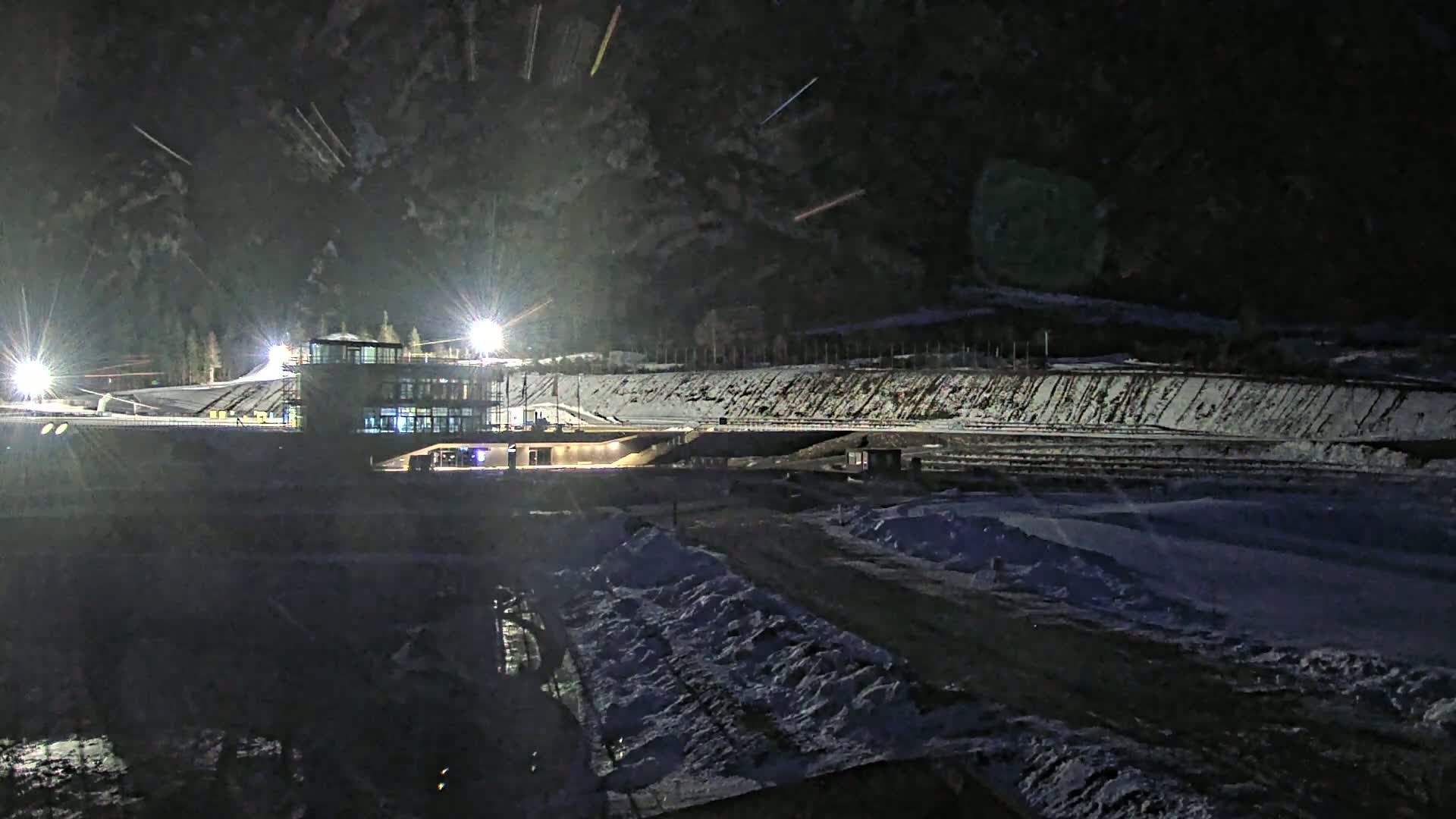 A brightly lit building sits beside a snow-covered, sloped track at night.