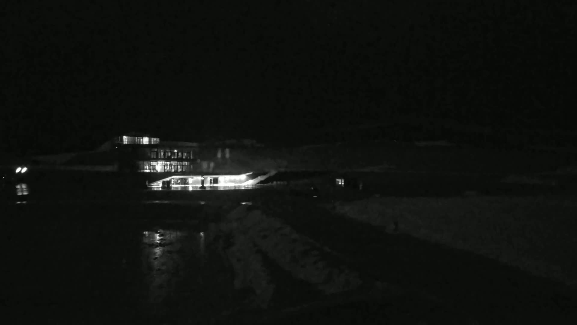 A brightly lit building is visible at night, with snow on the ground in the foreground.