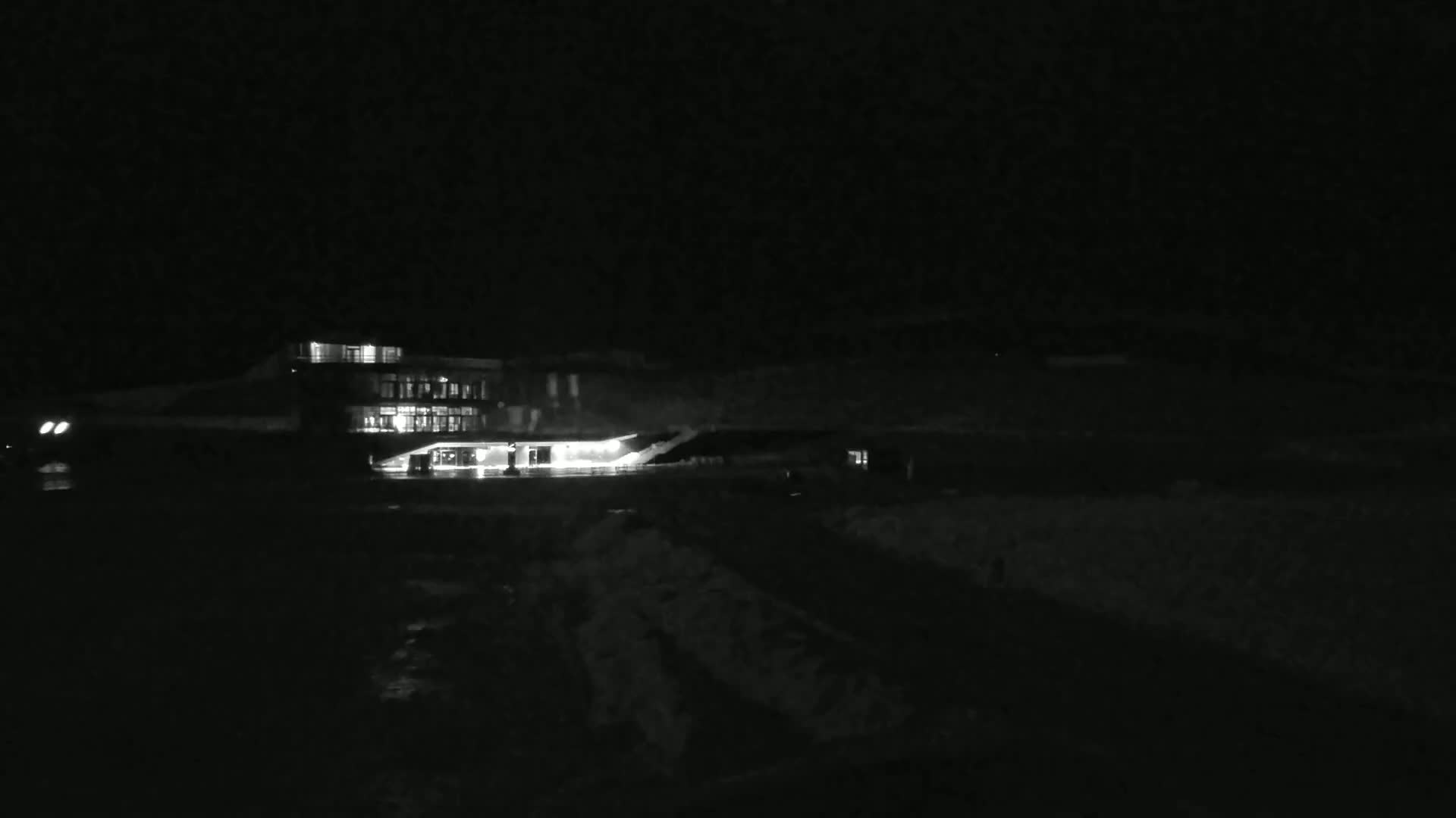 A brightly lit building sits on a dark, snow-covered landscape at night.