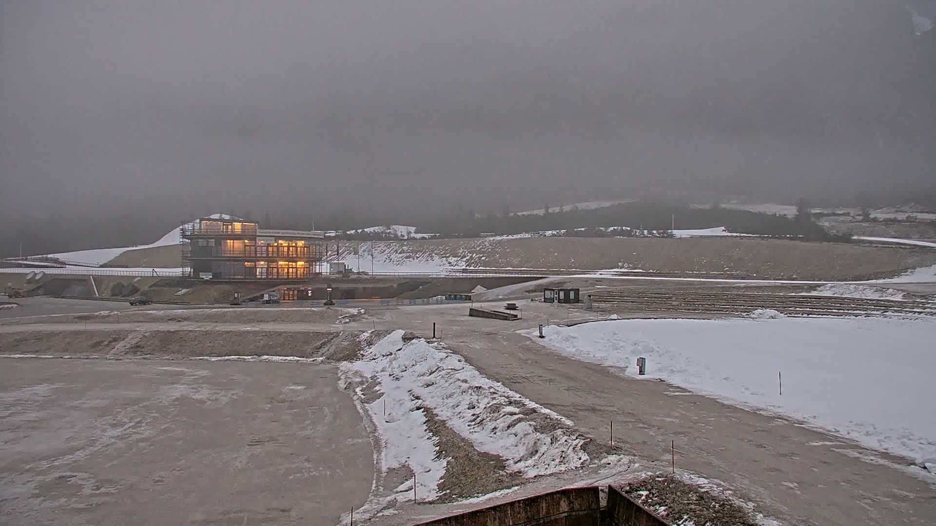 A partially-constructed building is illuminated in the foreground of a snow-dusted, overcast landscape.