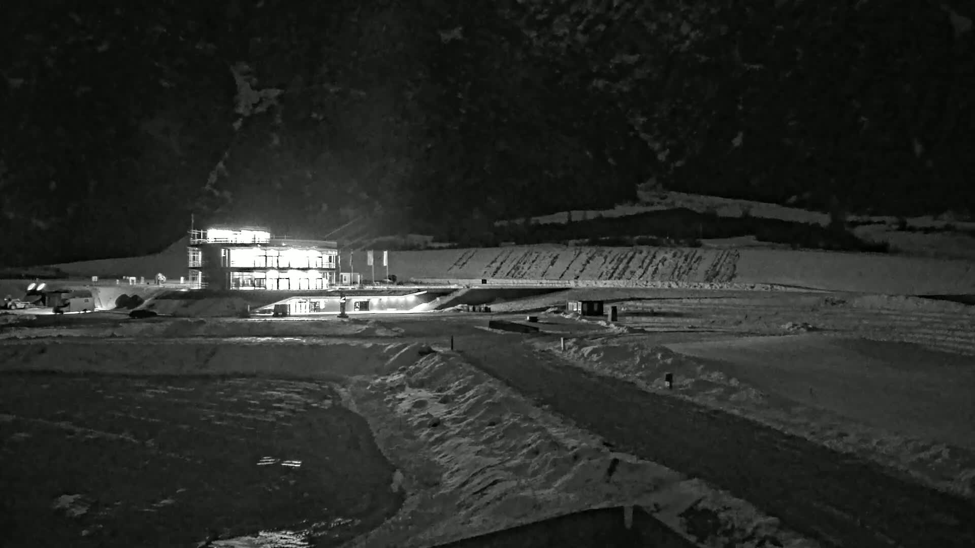 A brightly lit building sits in a snow-covered landscape at night, under a dark sky.