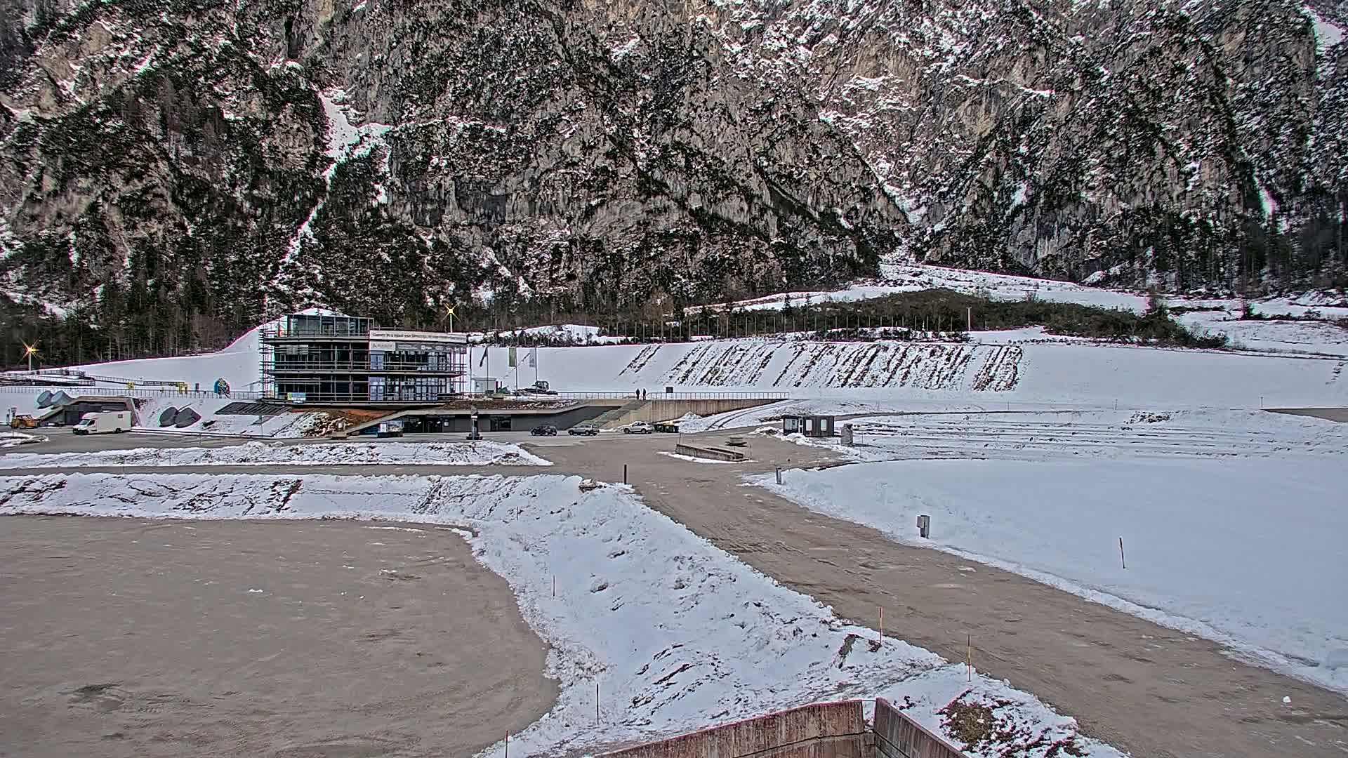 A modern building sits near a snowy, hilly landscape, with a large snow-covered area in the foreground.