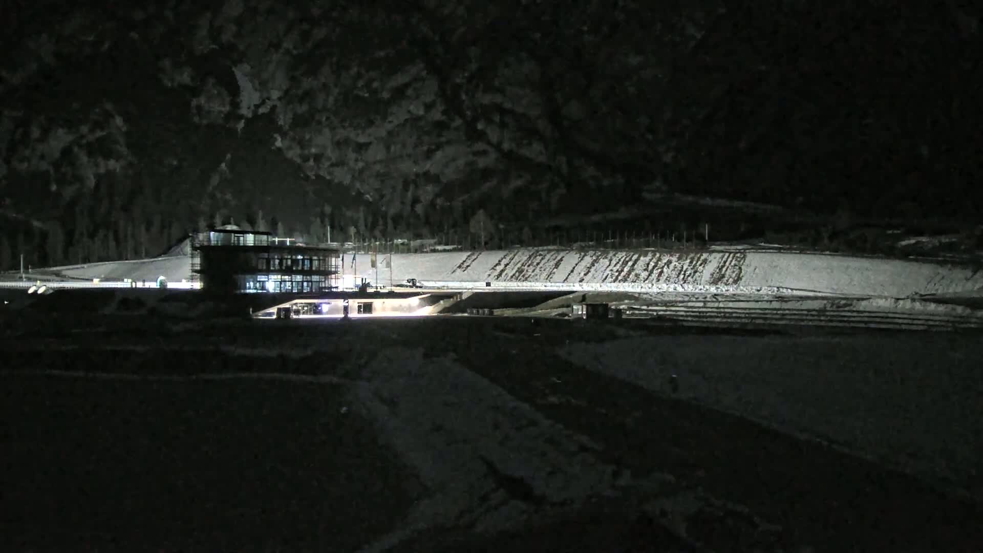 A lit building sits near a snow-covered, sloped track at night.