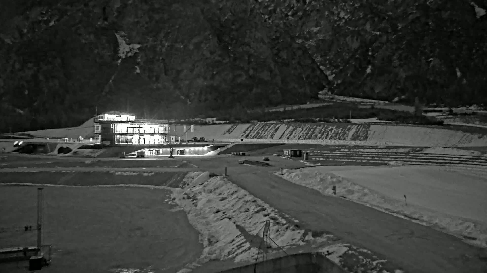 A brightly lit building sits at the base of a snow-dusted mountain at night.