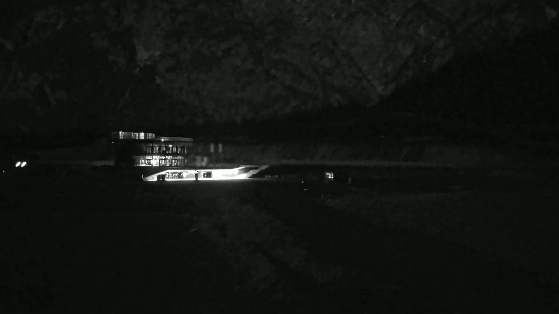 A brightly lit building is visible at night against a dark, mountainous background.