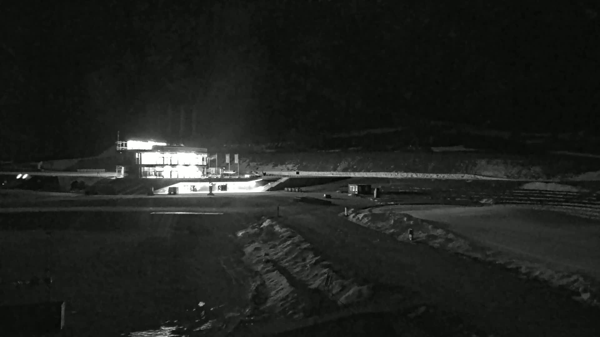 A brightly lit building stands at the edge of a dark, snow-covered field at night.