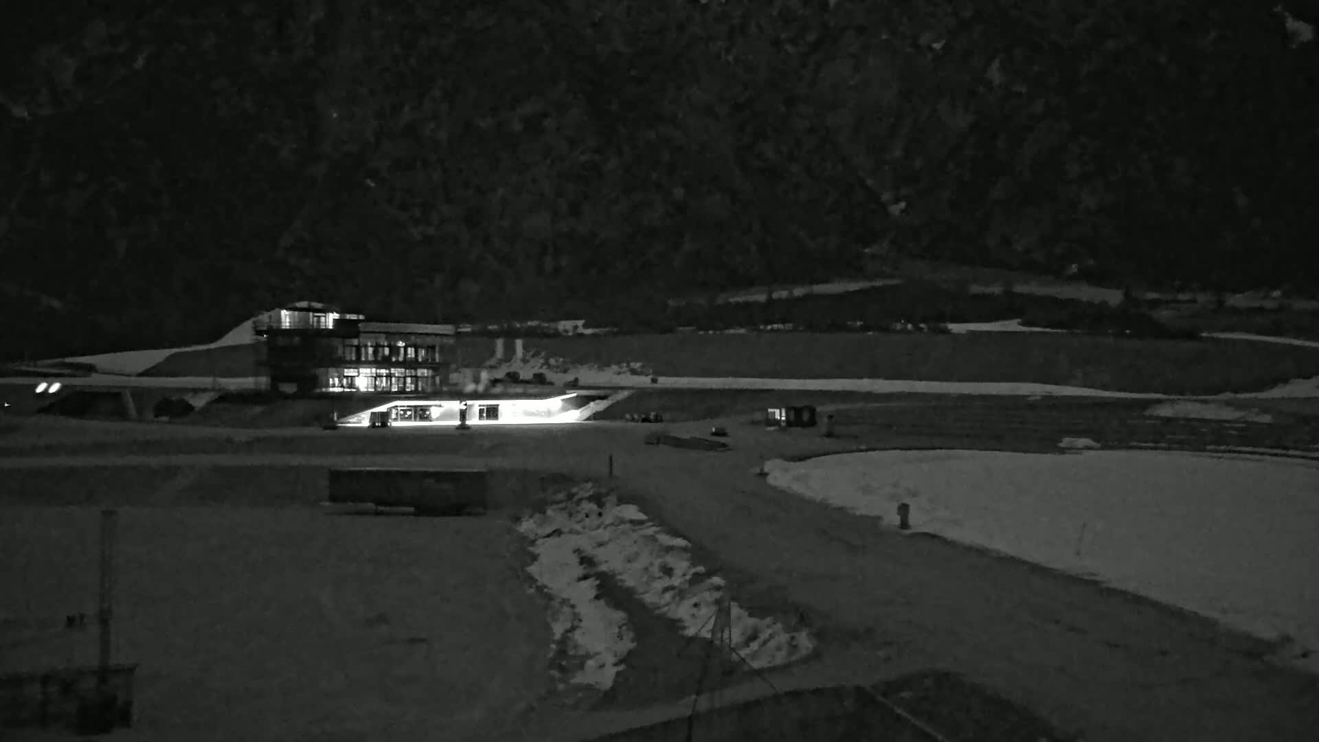 A brightly lit building sits in a snow-covered, dark landscape at night, with a mountain in the background.