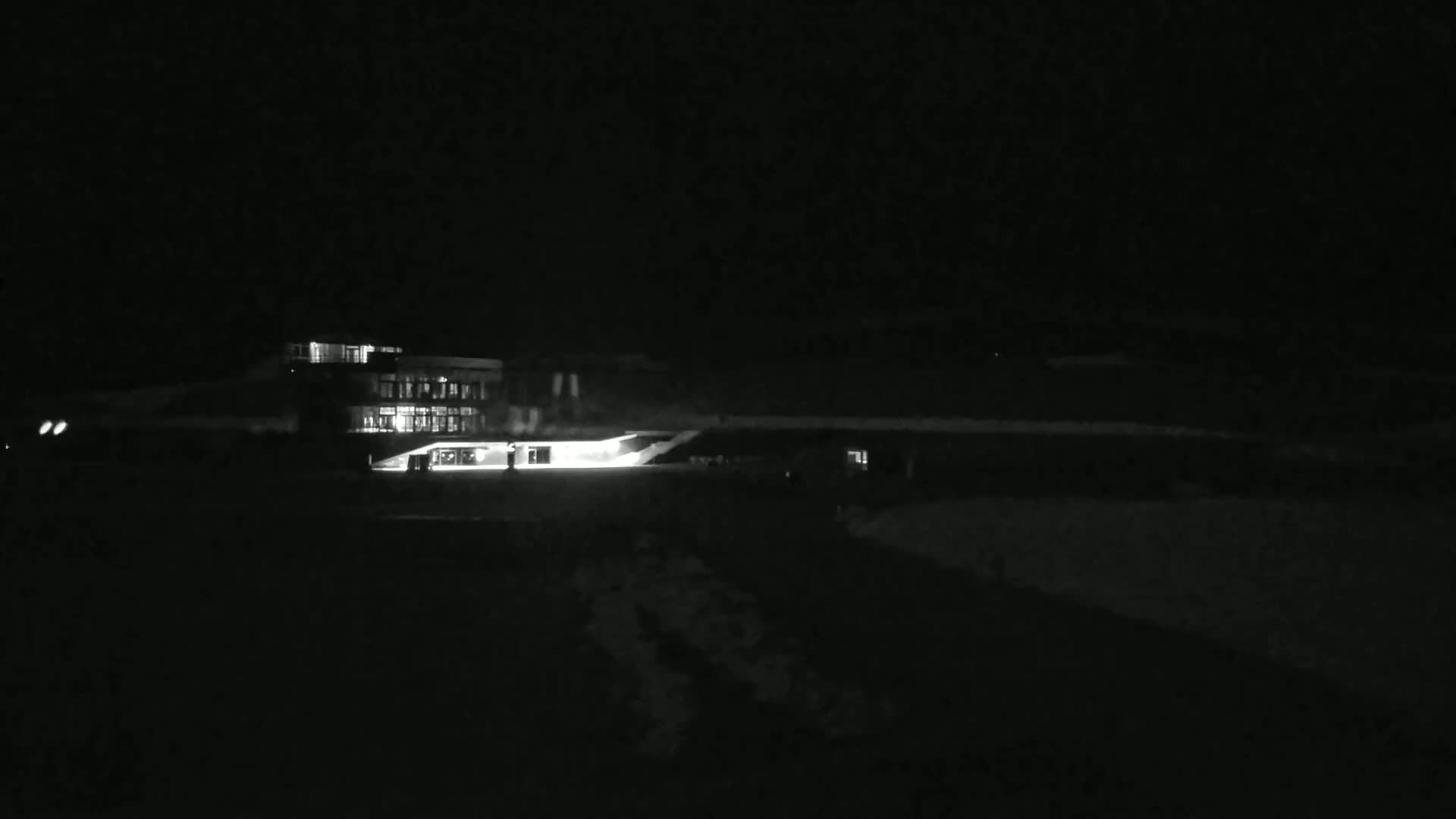 A brightly lit building is visible at night, surrounded by a dark, snow-covered landscape.
