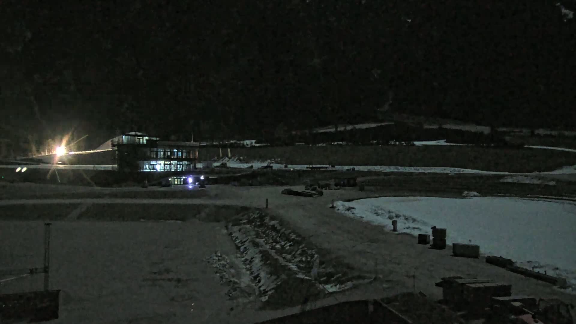 A brightly lit building sits in a snow-covered area at night, under a dark sky.