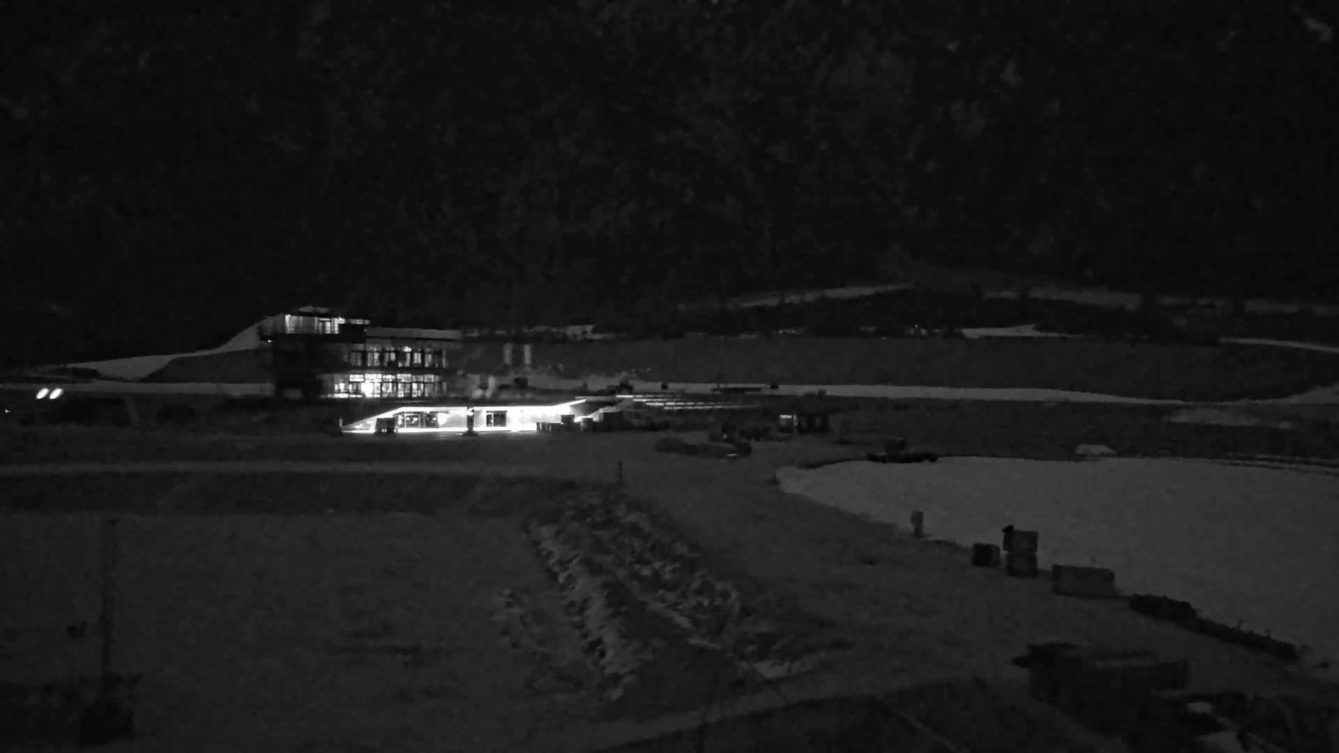 A brightly lit building sits on a snow-covered landscape at night, under a dark sky.