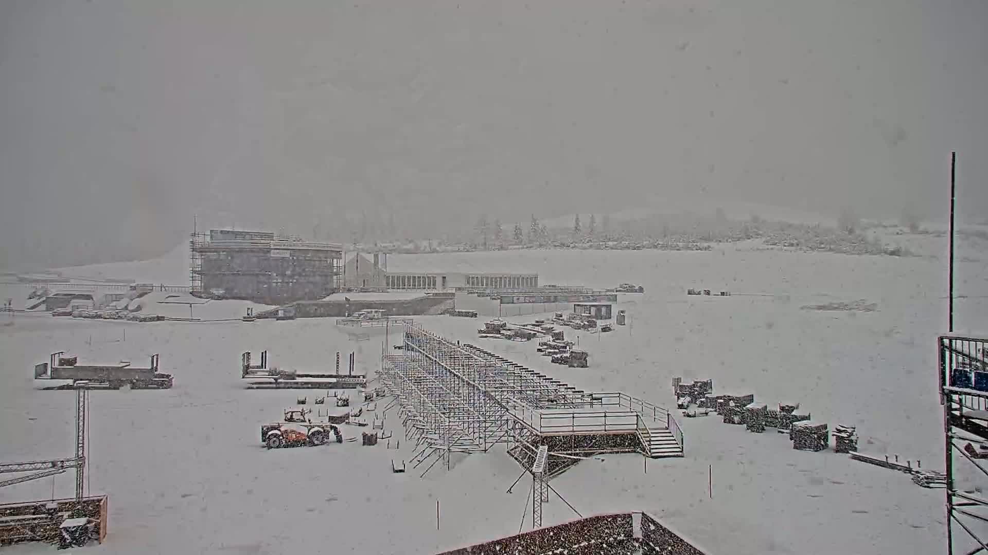 A snow-covered construction site with buildings and scaffolding is visible during a heavy snowfall.