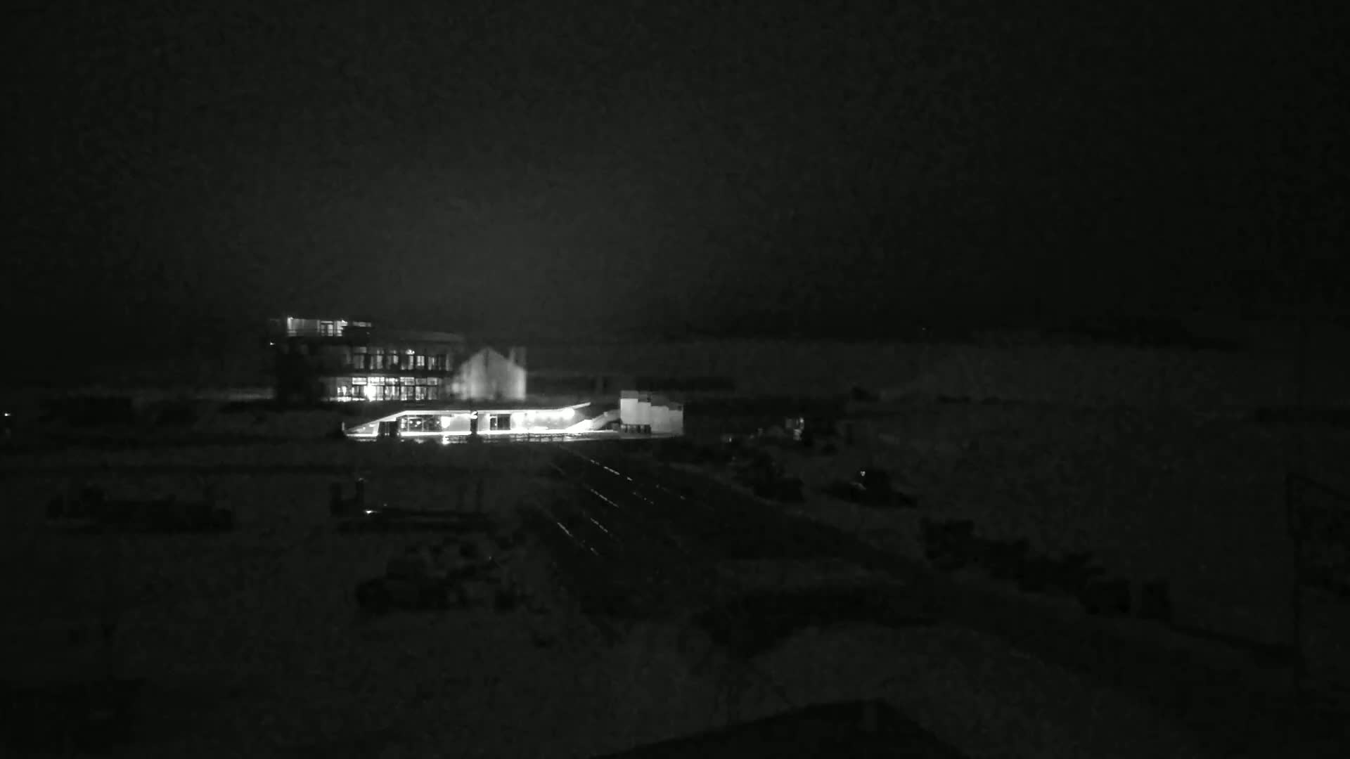 A brightly lit building is visible at night in a snowy landscape under a dark sky.