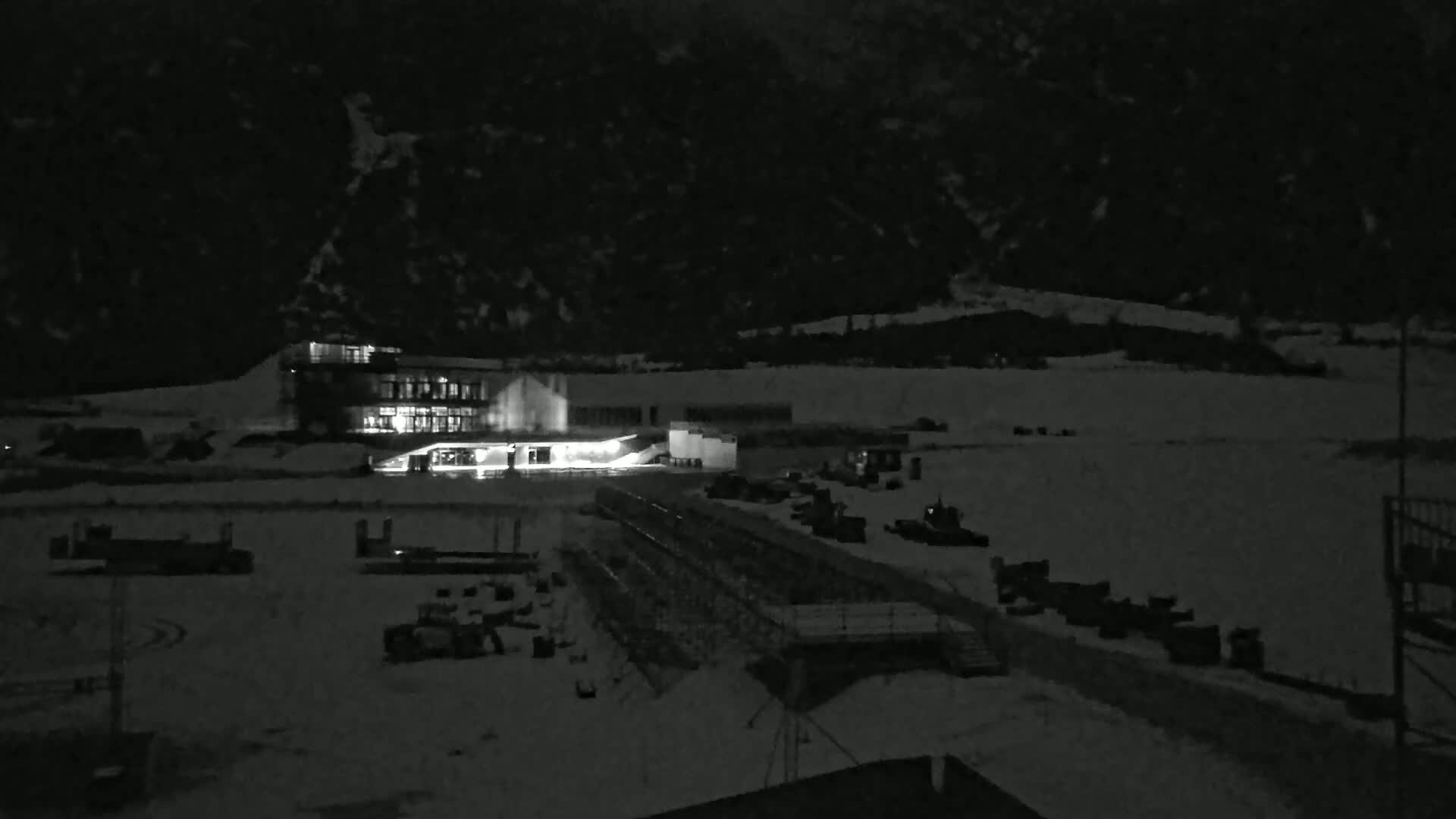 A brightly lit building sits on a snow-covered landscape at night,  with mountains visible in the background.