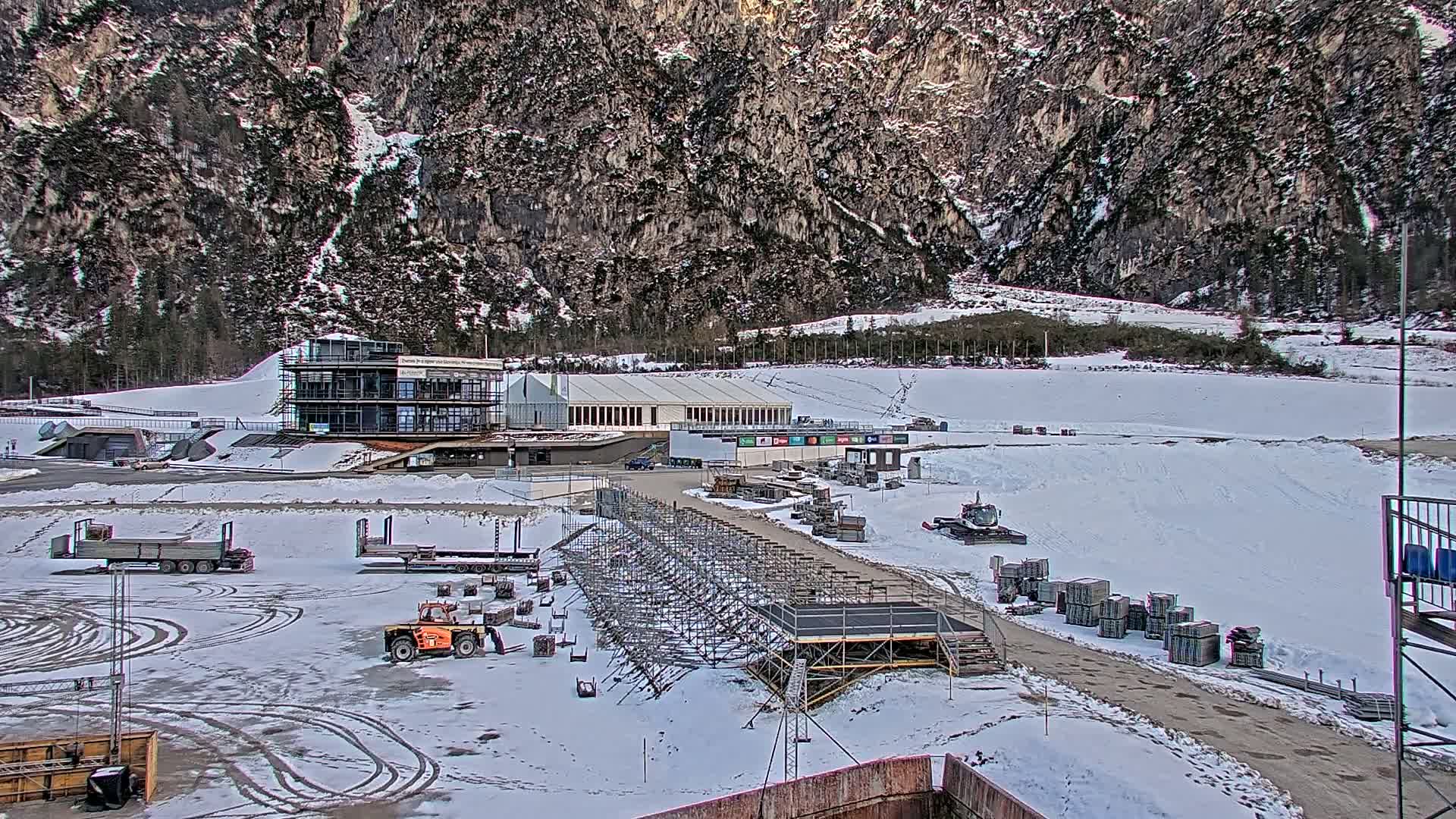 A snowy outdoor scene shows a partially-constructed building complex against a backdrop of a large, snow-dusted mountain.