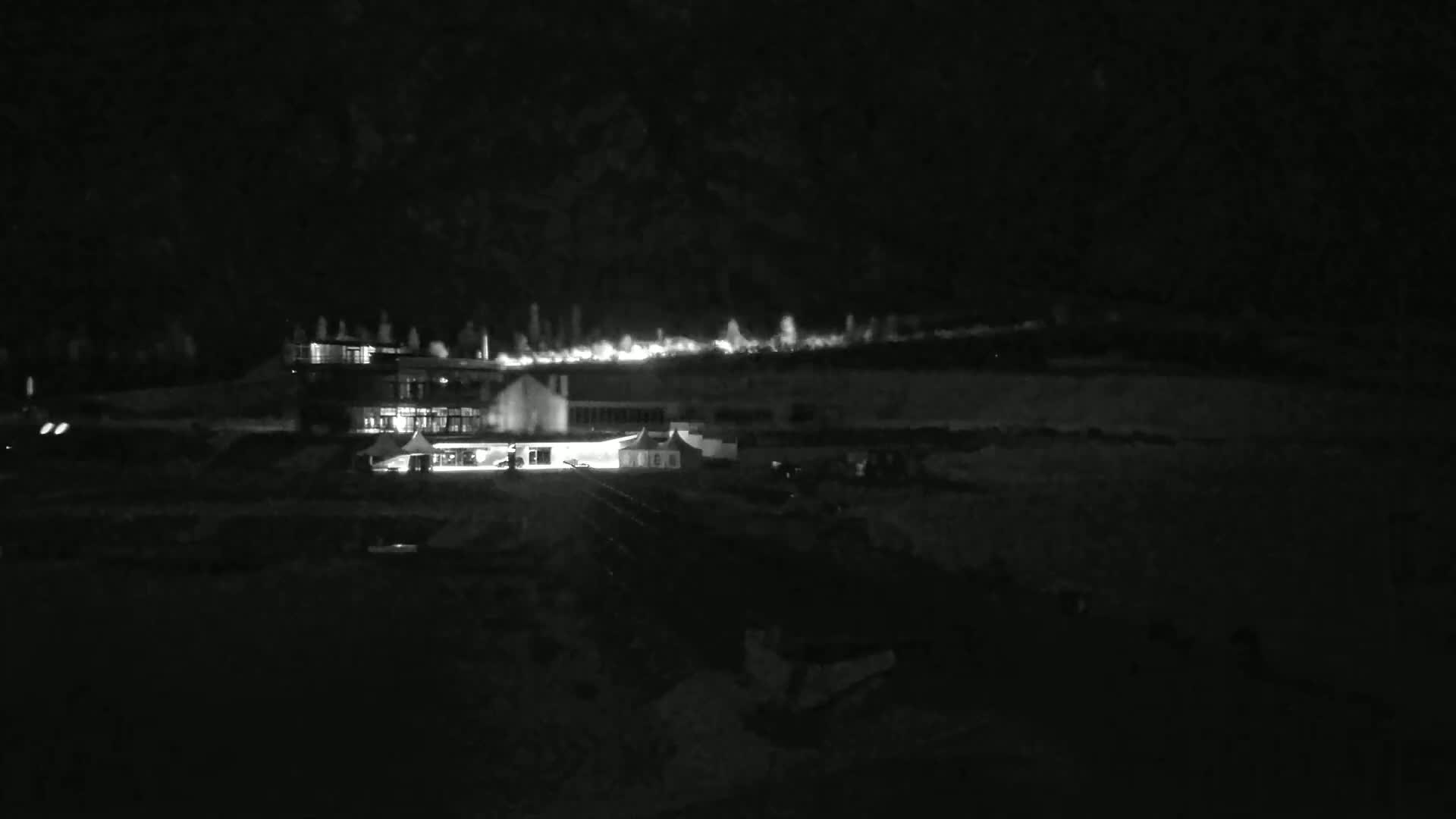 A brightly lit building complex sits on a dark hill at night, under a clear, dark sky.