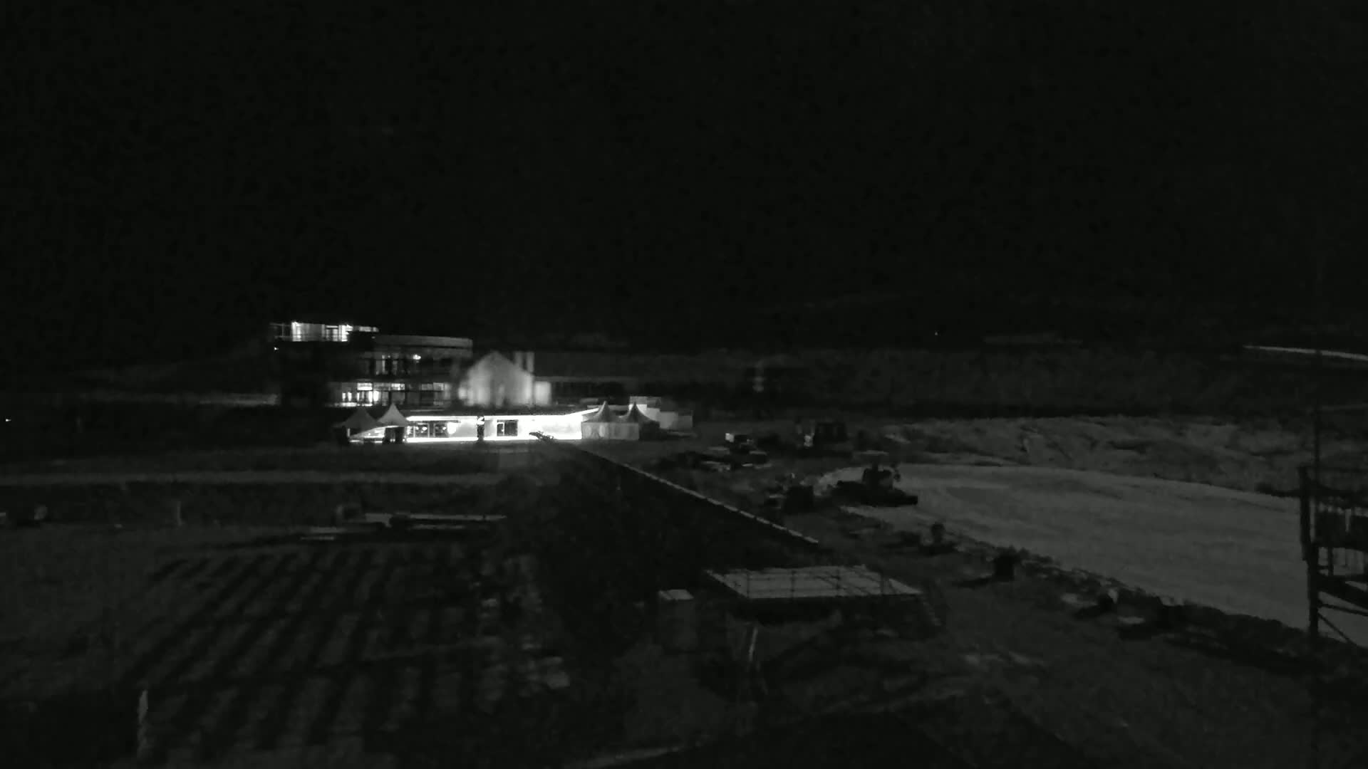 A brightly lit building and a tent are visible at night, along with a mostly dark, snow-covered landscape.