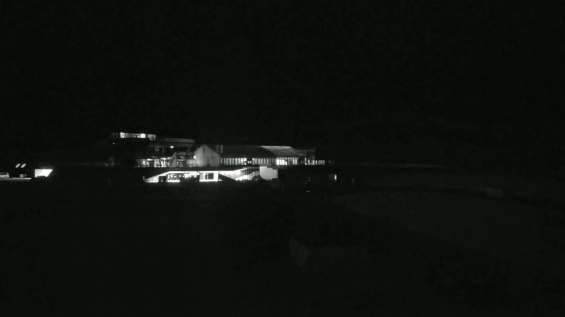 At night, a brightly lit building complex sits in a dark, seemingly empty landscape.