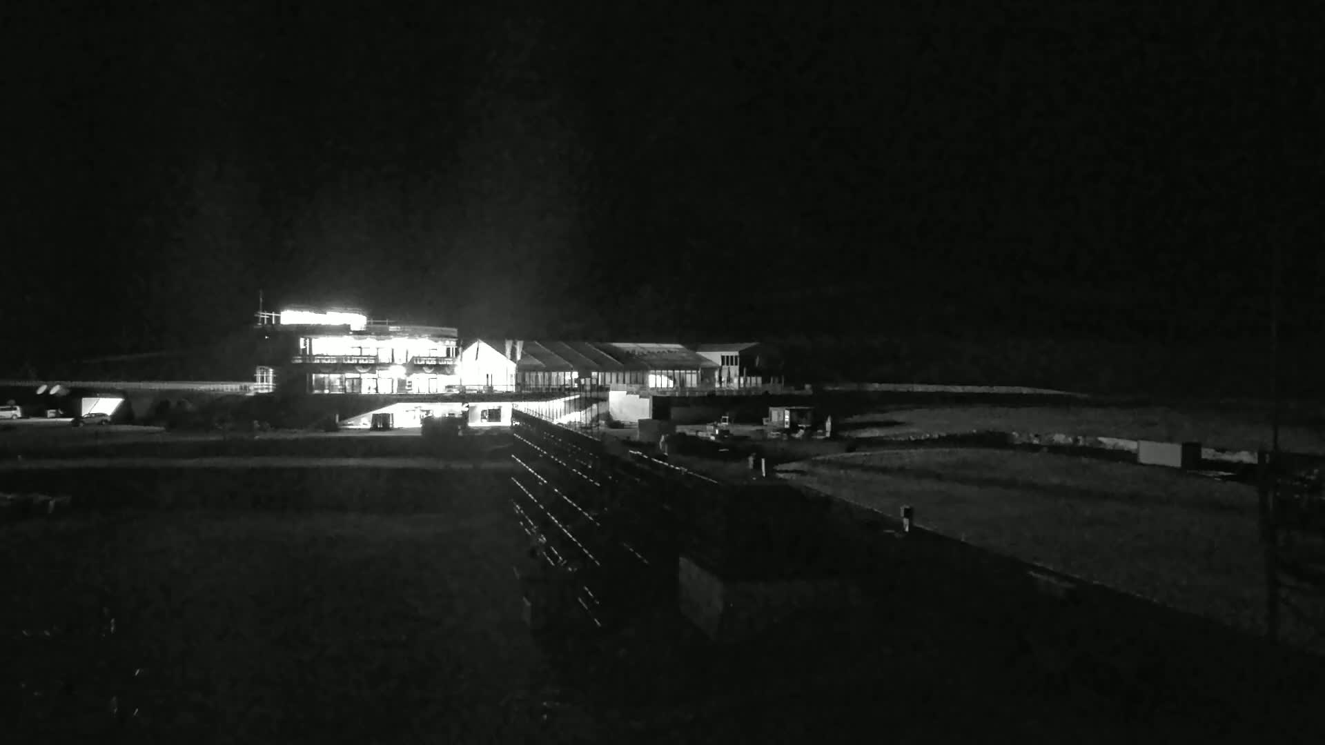 At night, illuminated buildings and vehicles are visible near a dark, possibly fenced-in area.