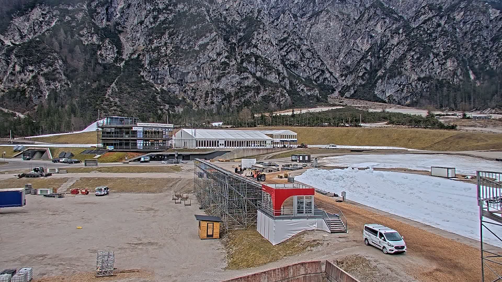 A partially snow-covered outdoor sports facility sits at the base of a large mountain range on an overcast day.