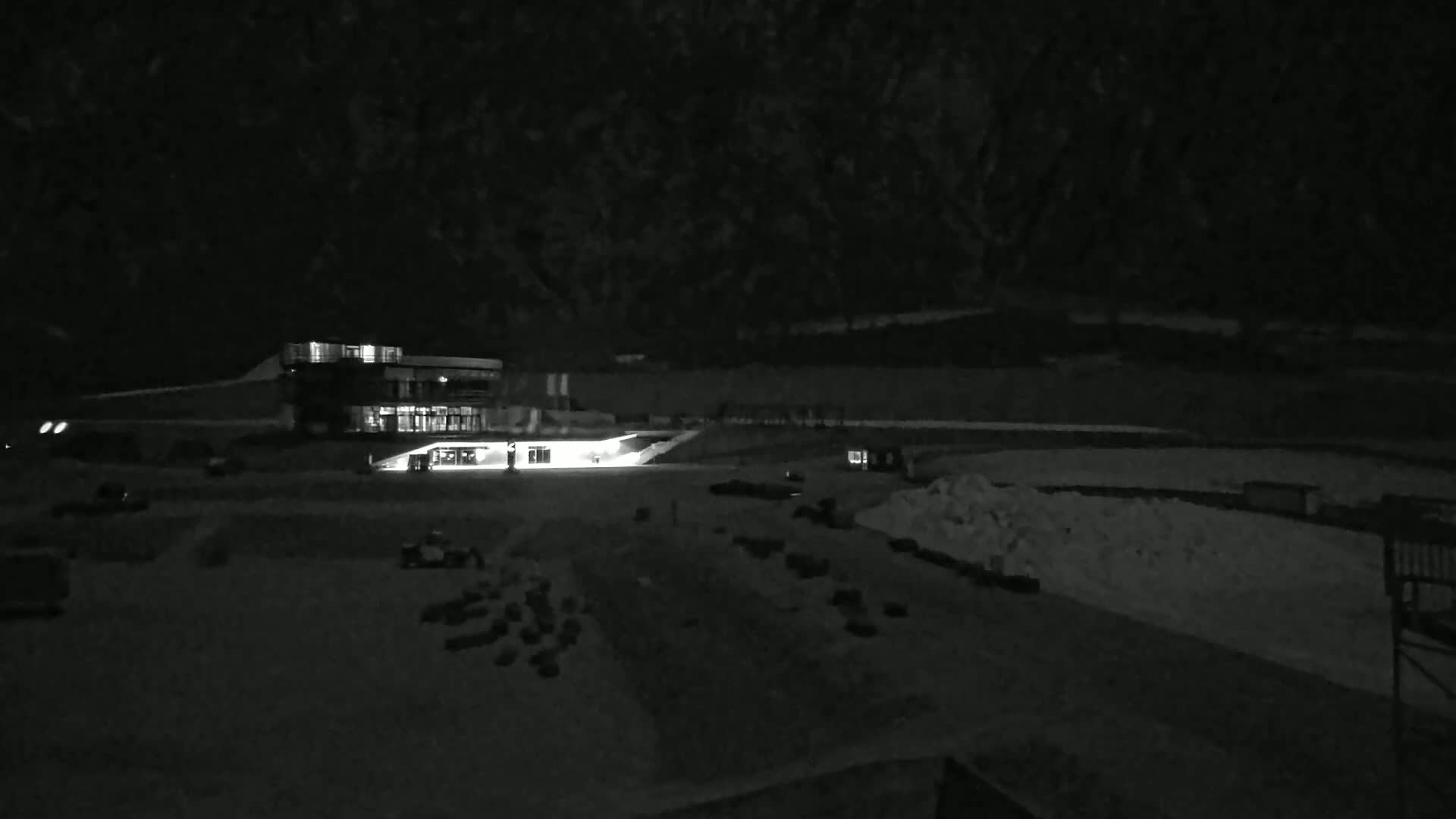 A brightly lit building sits in a snow-covered, dark area at night.