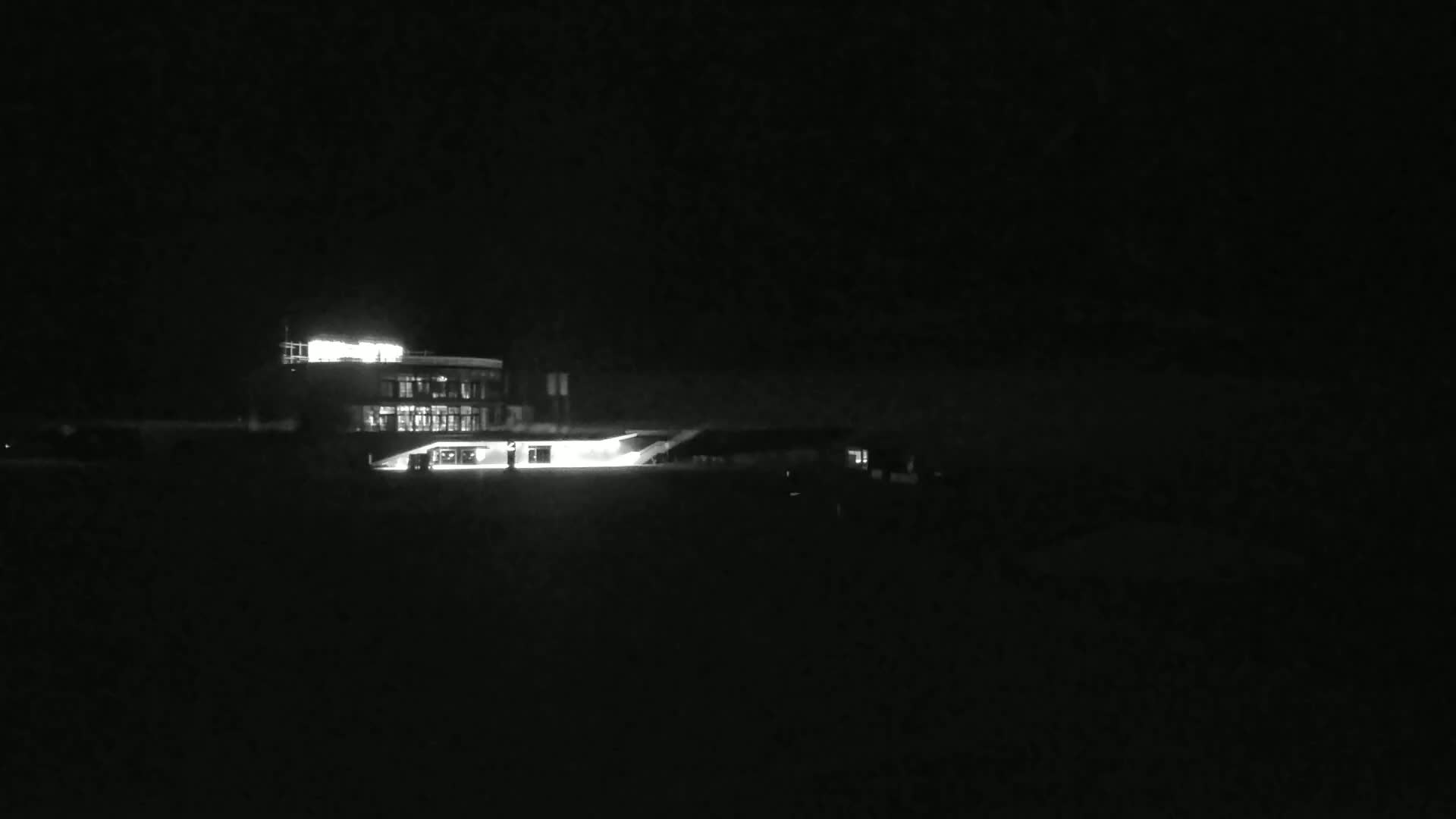 A brightly lit building is visible at night, with a dark, possibly snowy, foreground.