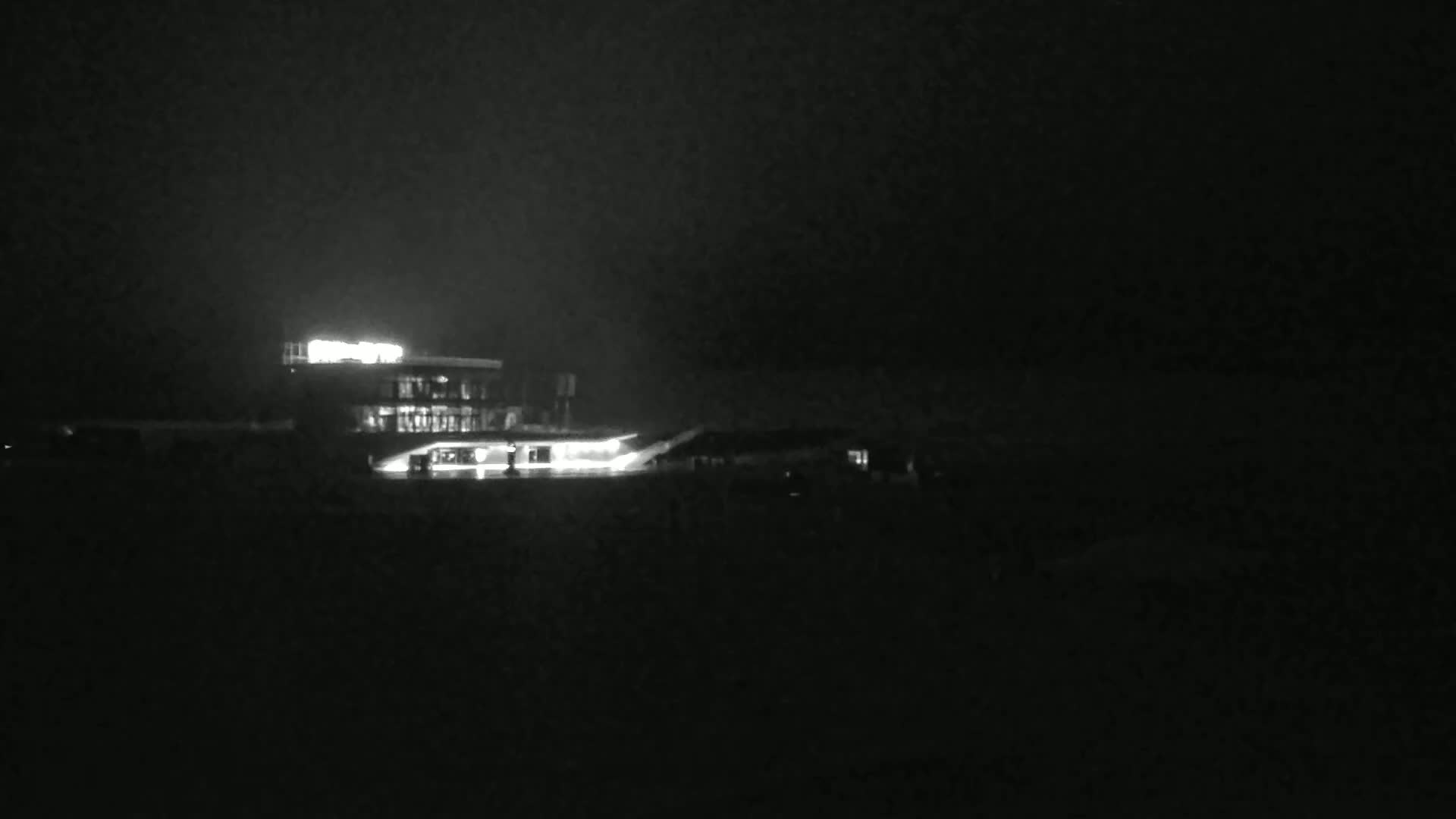 A brightly lit building is visible at night in dark, overcast conditions.