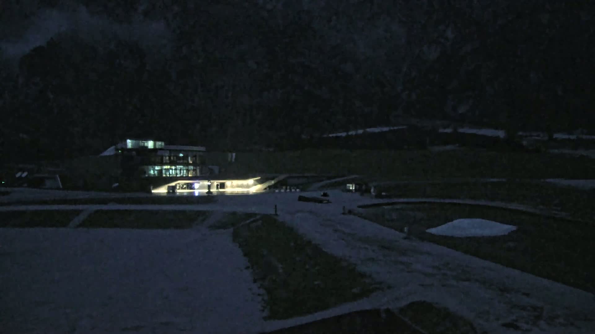 A lit building sits on a snow-covered landscape at night, under a dark, possibly snowy sky.