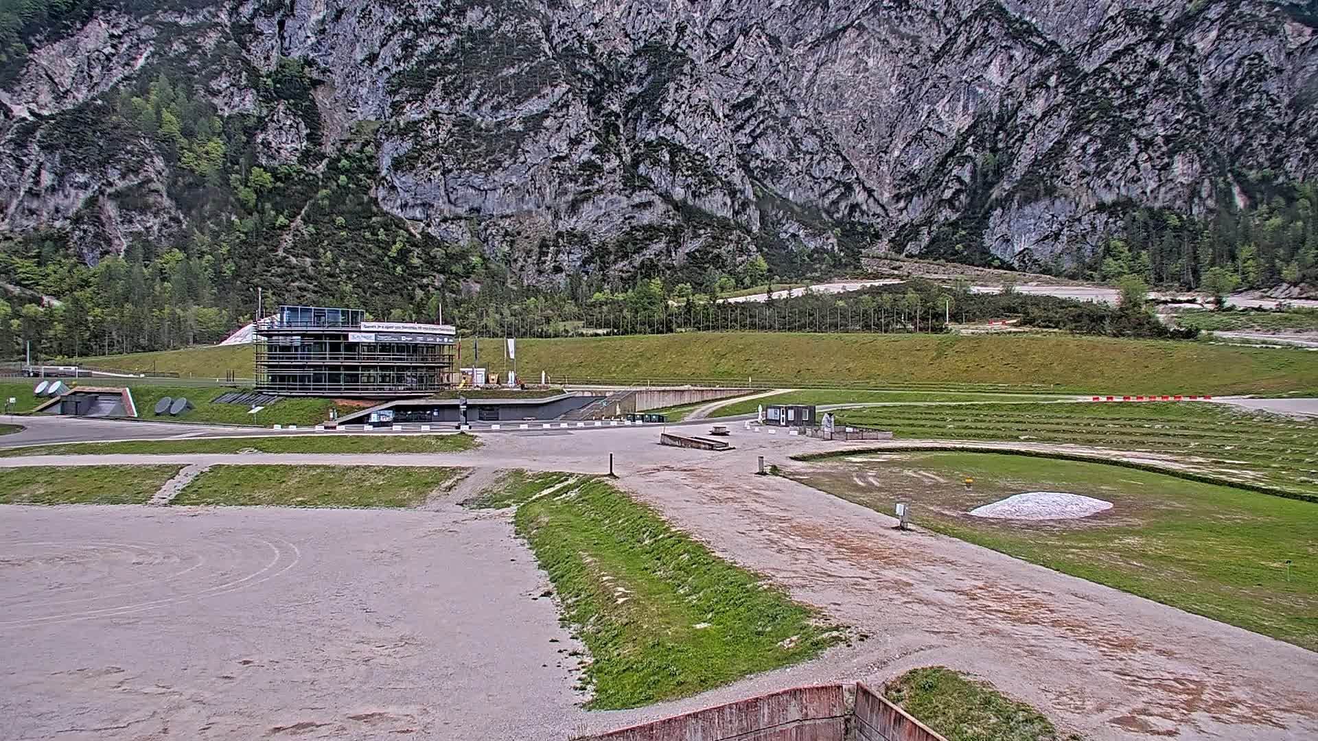 A multi-story building sits in an outdoor sports complex nestled against a large, grey mountain under an overcast sky.