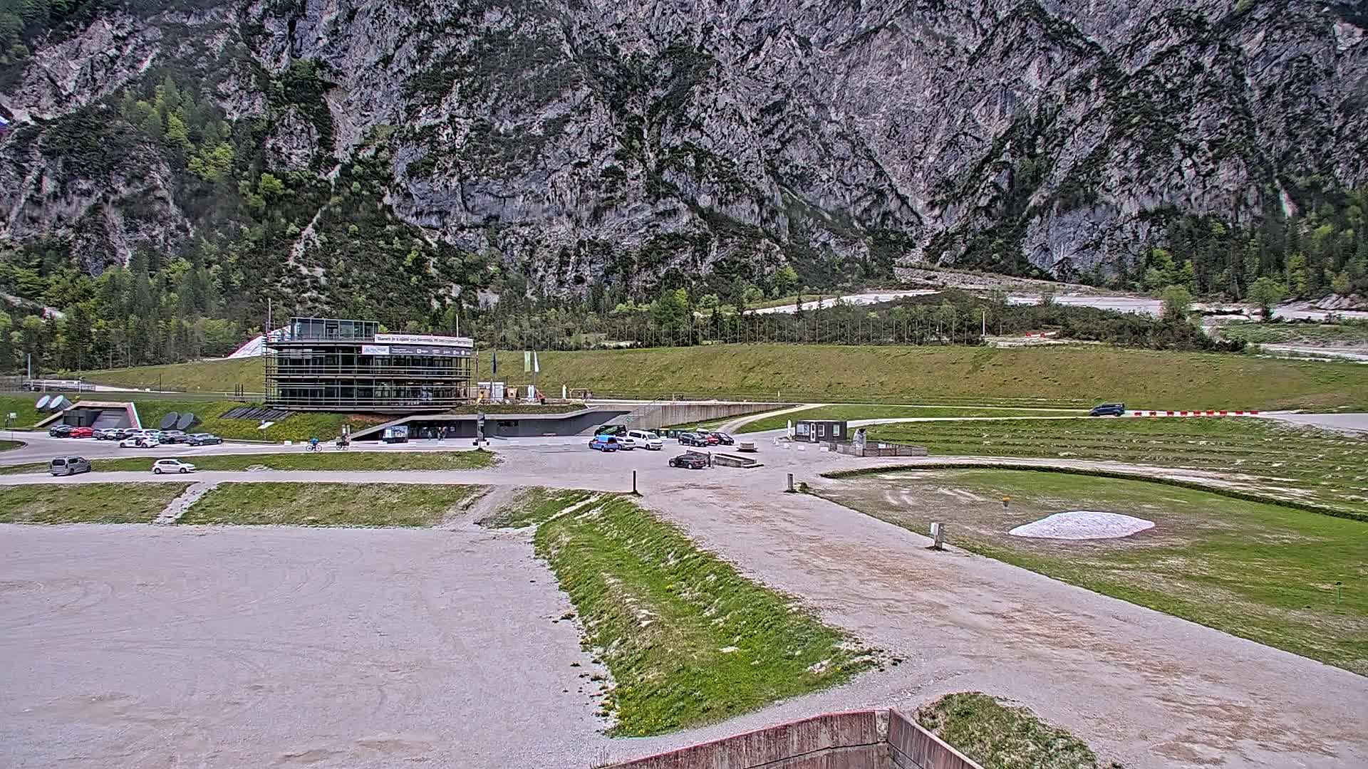 A modern building sits in a parking lot at the base of a large, gray mountain under a cloudy sky.
