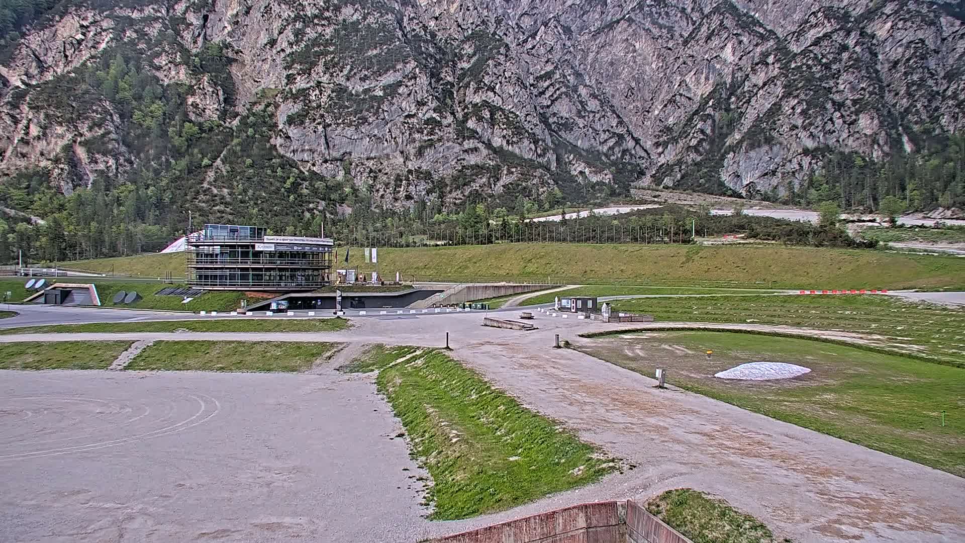 A large building sits near the base of a mountain on an overcast day, with a paved area and grassy patches in the foreground.