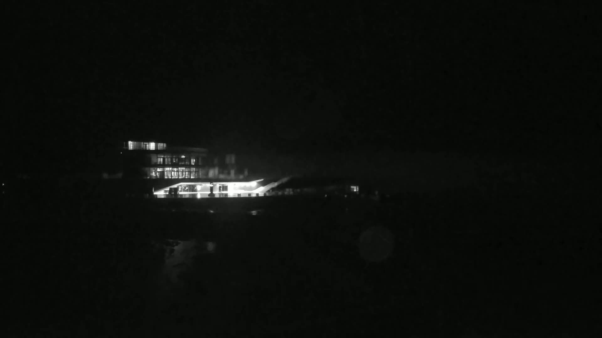 A brightly lit building is visible at night, surrounded by darkness.