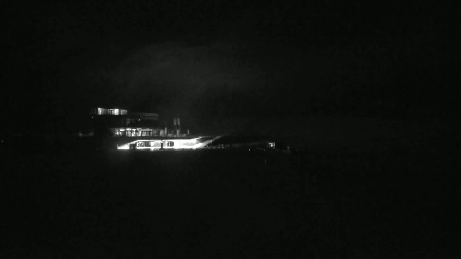 A brightly lit building is visible at night under a dark, cloudy sky.