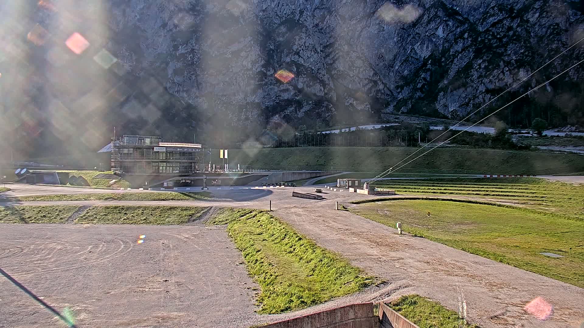 A modern building sits at the base of a large, rocky mountain on a mostly sunny day with some lens flare.