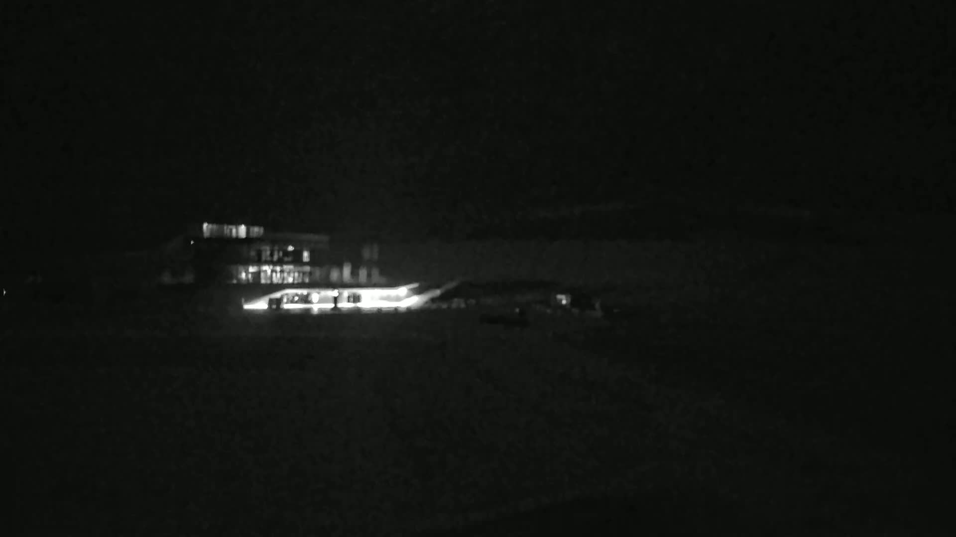 A brightly lit building is visible at night, with a dark, possibly snowy, foreground.