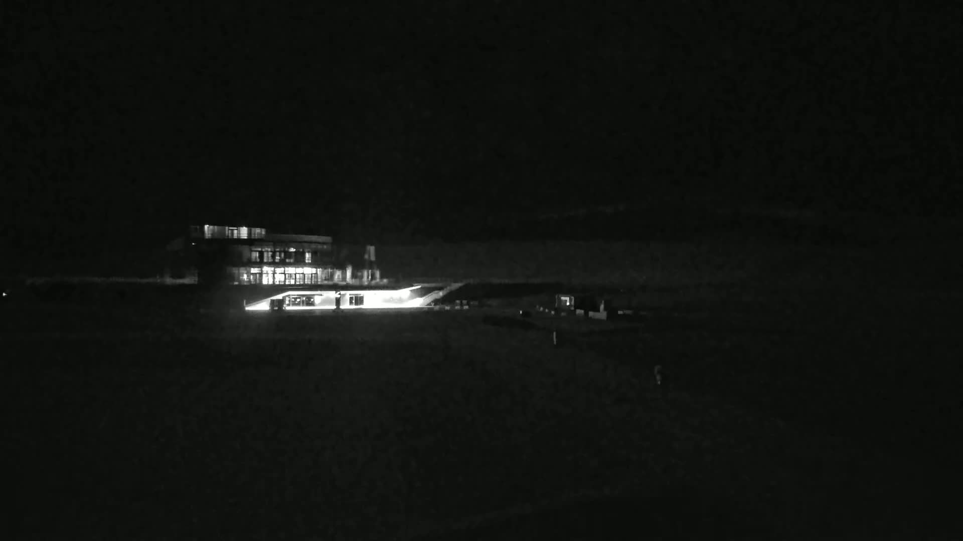 A brightly lit building sits in a dark, nighttime landscape.
