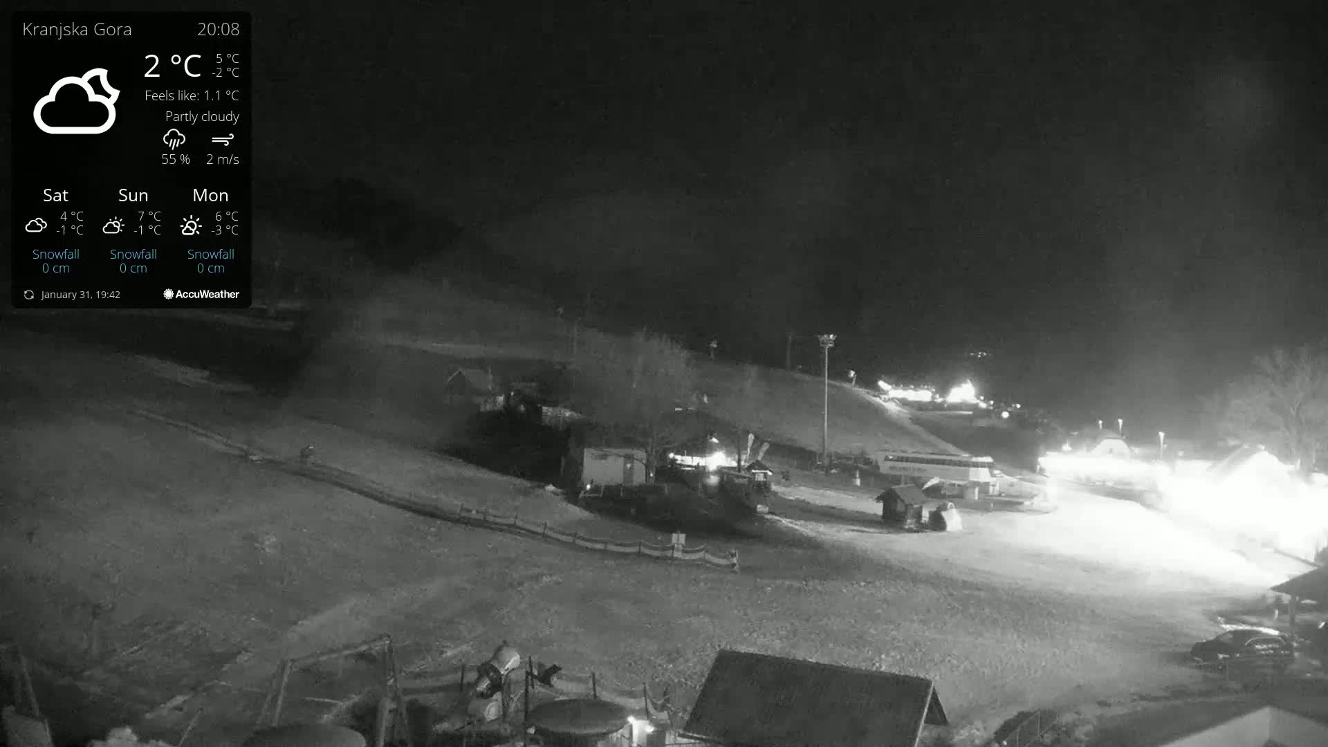 A nighttime, partly cloudy view of a snow-covered ski slope with buildings and lights visible.