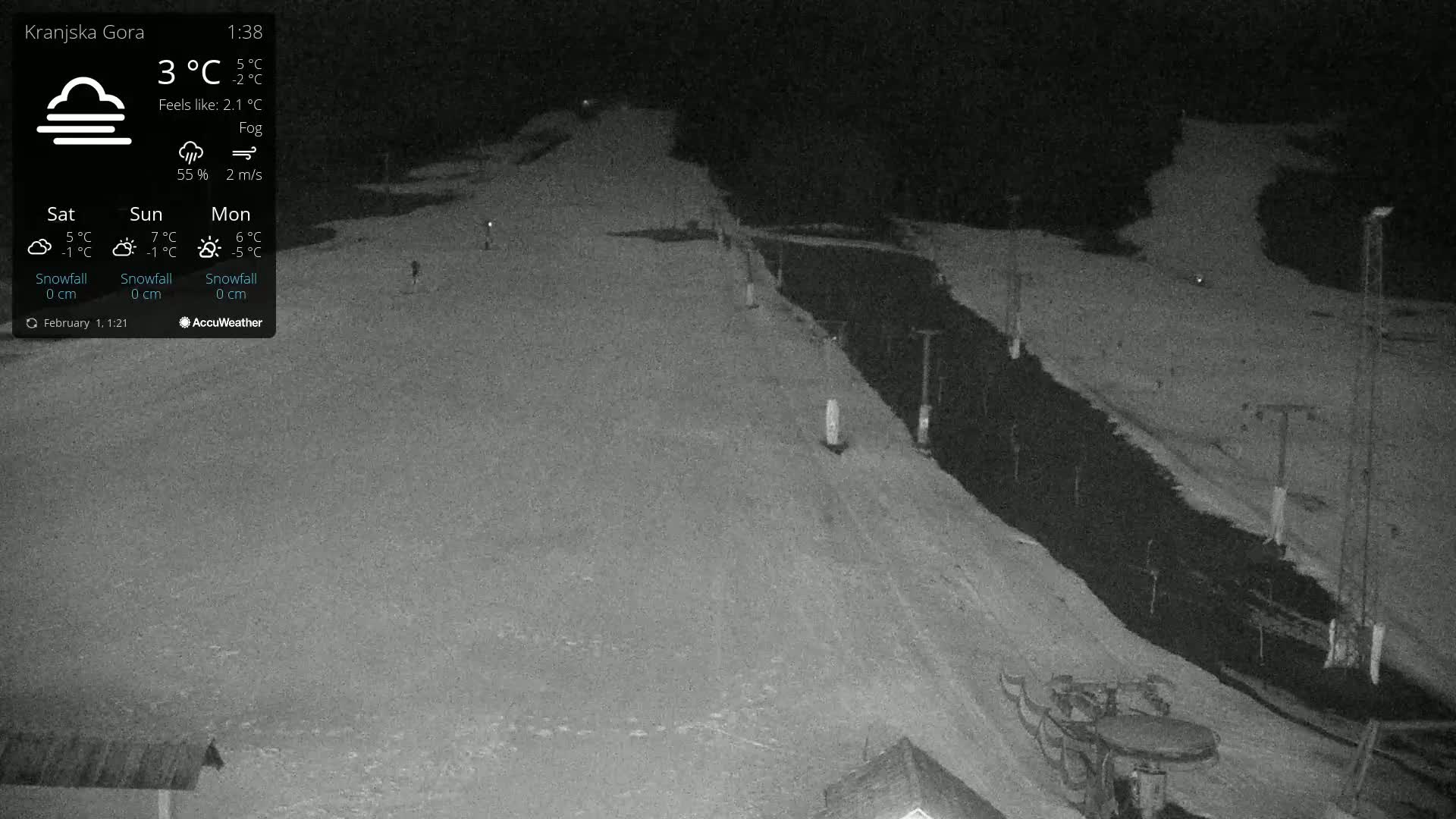 A nighttime, foggy view of a snow-covered ski slope with some ski lift infrastructure visible.