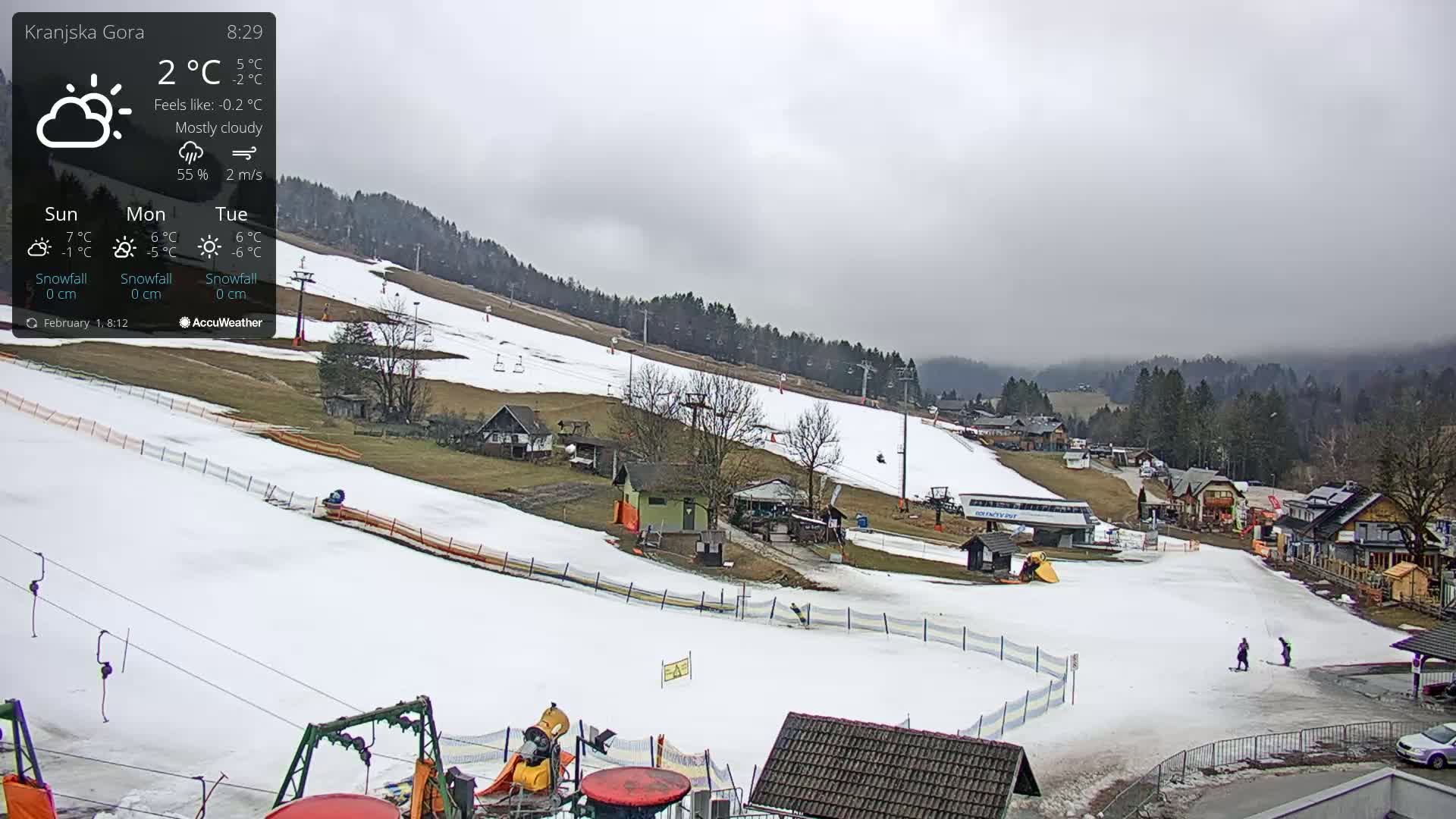 A mostly cloudy day at a snow-covered ski resort, with several ski lifts and buildings visible.