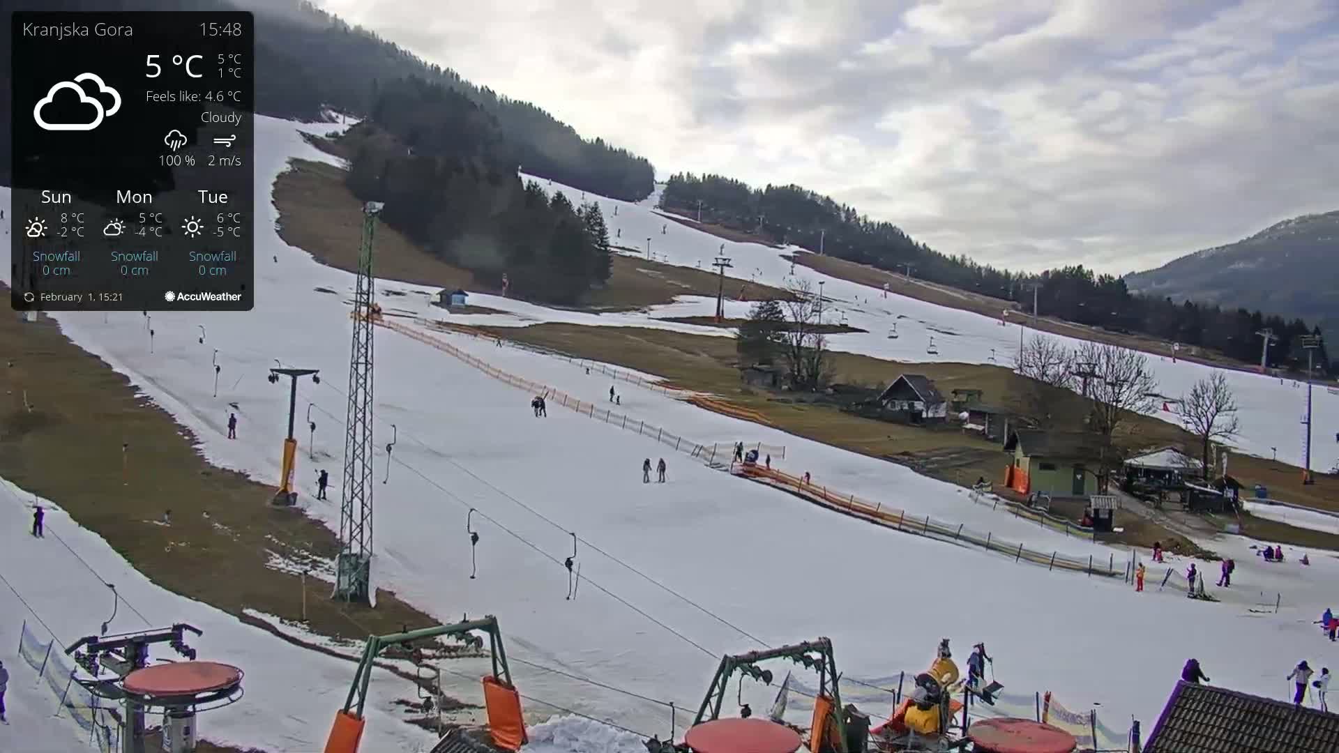 A cloudy day at a ski resort shows several skiers and snowboarders on a snow-covered slope with ski lifts visible.