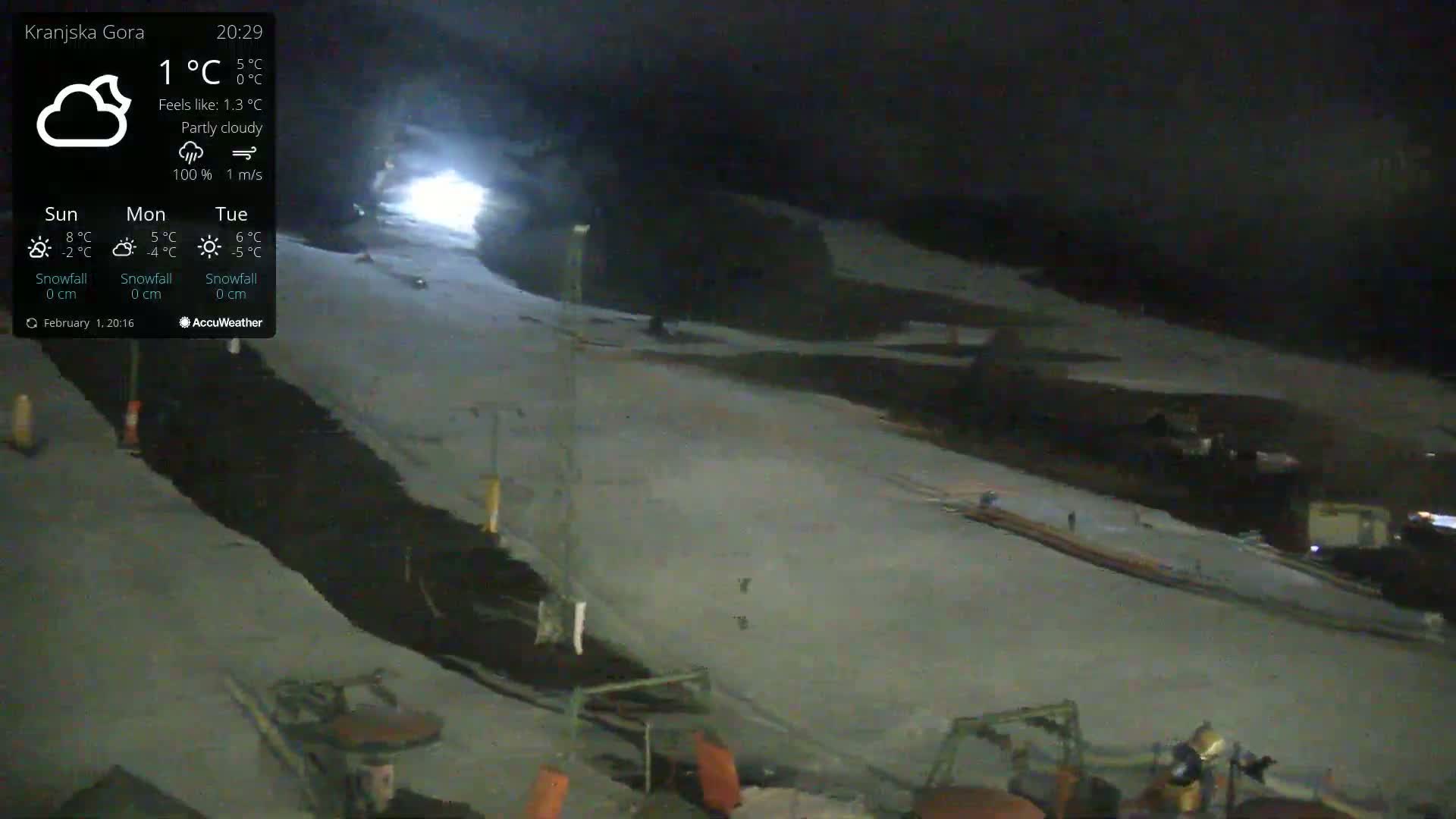 A snow-covered ski slope is illuminated at night under partly cloudy skies.