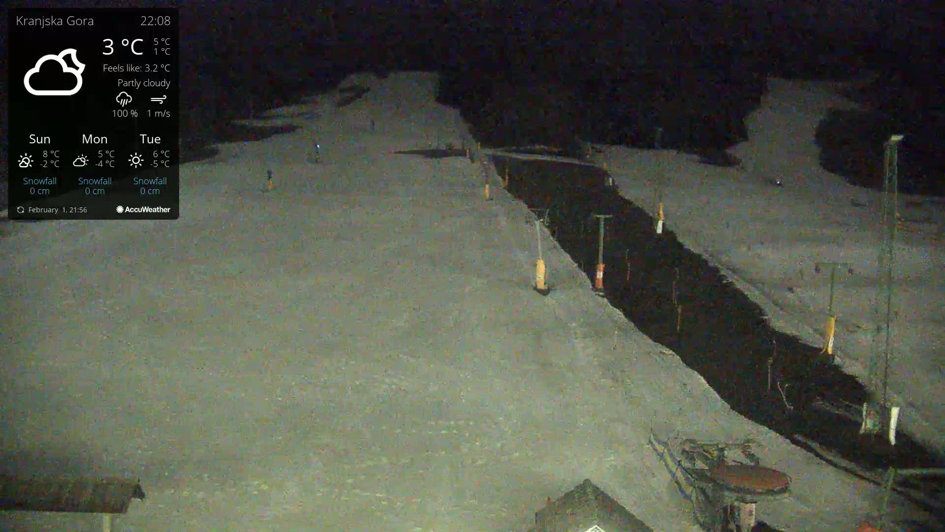 A nighttime, partly cloudy view of a snow-covered ski slope with a dark, narrow path running through it.