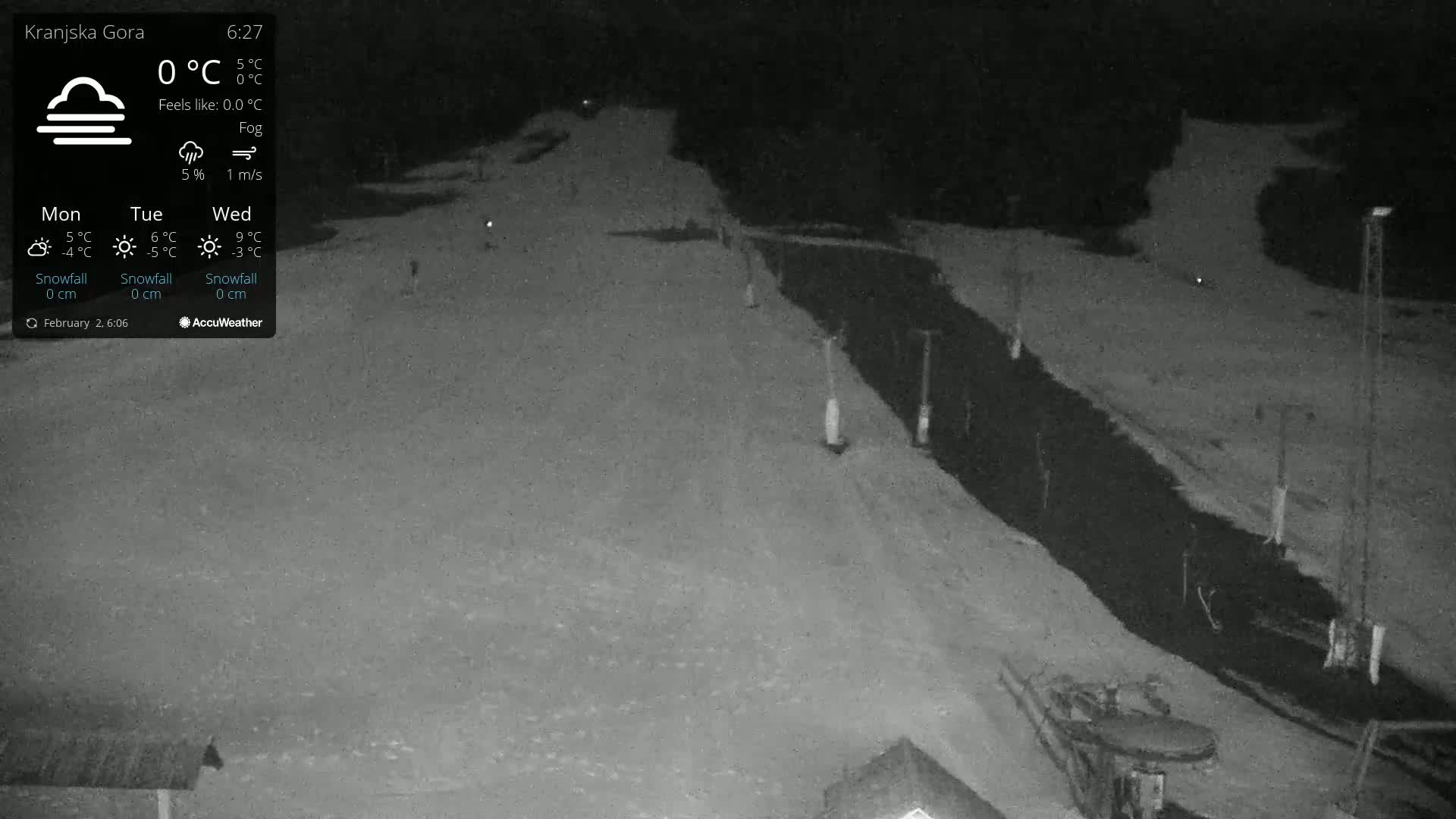 A nighttime, foggy scene shows a snow-covered area with a dark, unpaved path or road next to it.