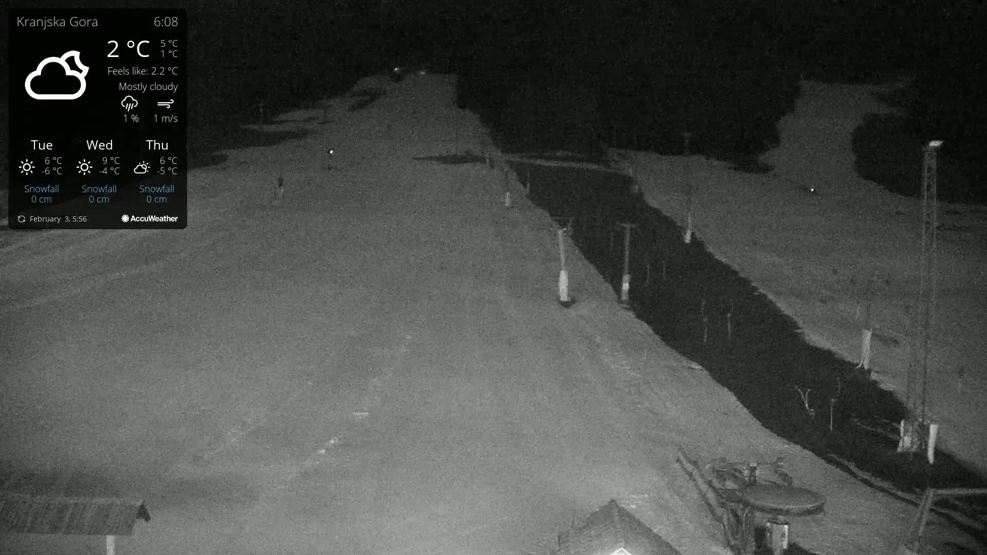 A nighttime, mostly cloudy view of a snow-covered slope with a dark road or path next to it.