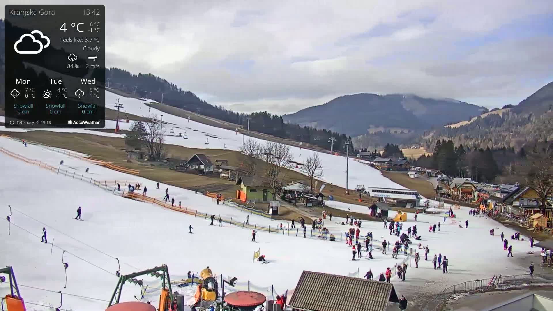 A snowy ski slope with people skiing and snowboarding under a cloudy sky.