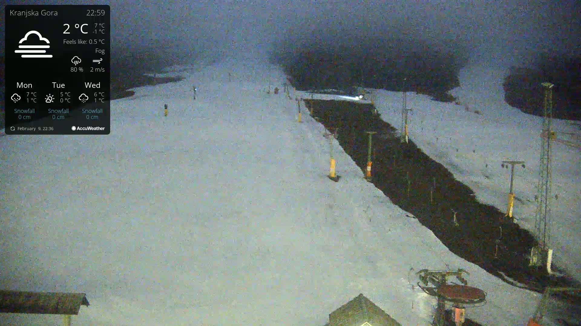 A snow-covered ski slope is visible at night under foggy conditions.