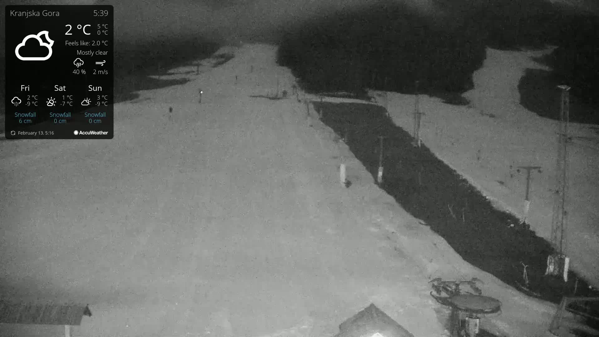 A mostly clear night scene shows a snow-covered ski slope with dark, unlit areas and some ski lift equipment visible under the night sky.