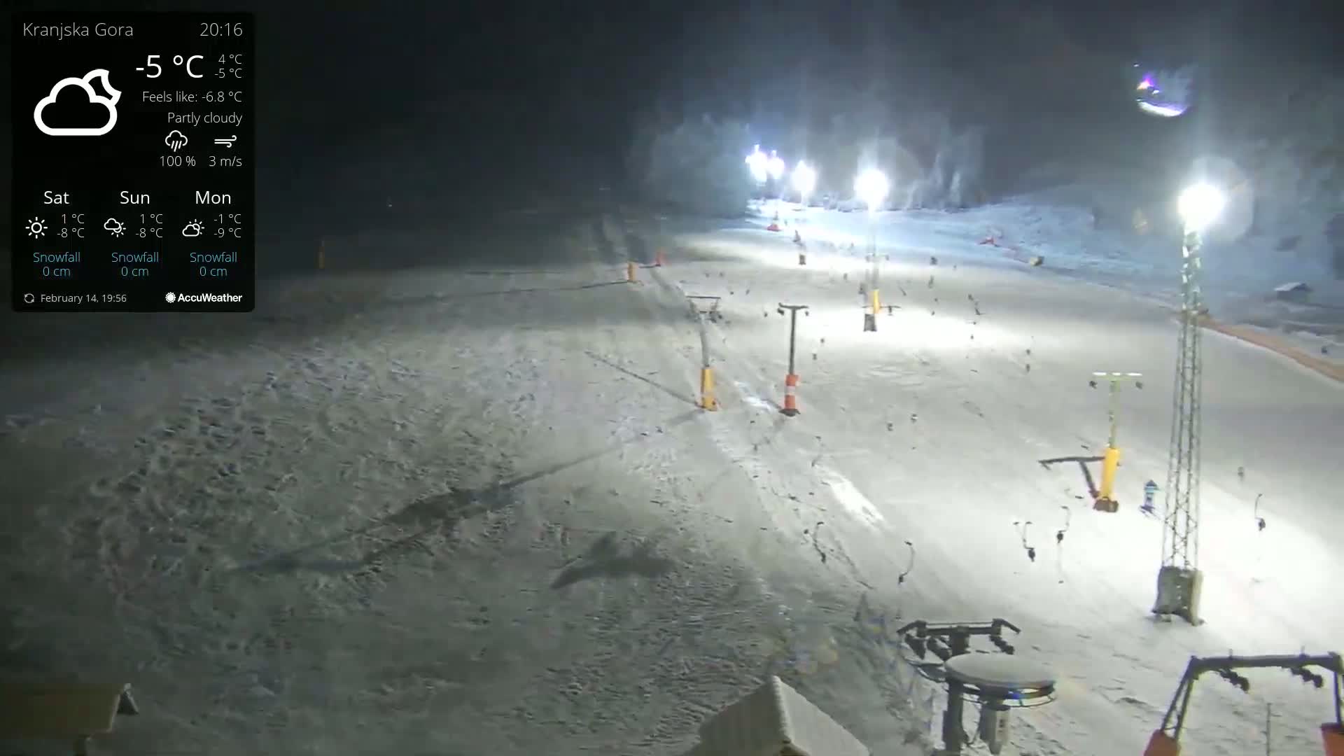 A nighttime, partly cloudy view of a snow-covered ski slope illuminated by floodlights, with several ski lifts and sparsely scattered skiers visible.