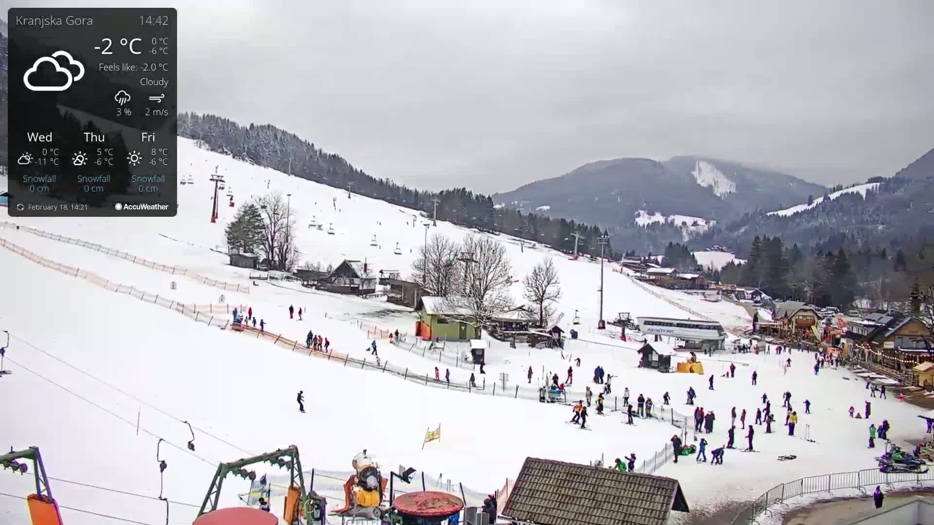 A snowy ski resort with many people skiing and snowboarding under cloudy skies.