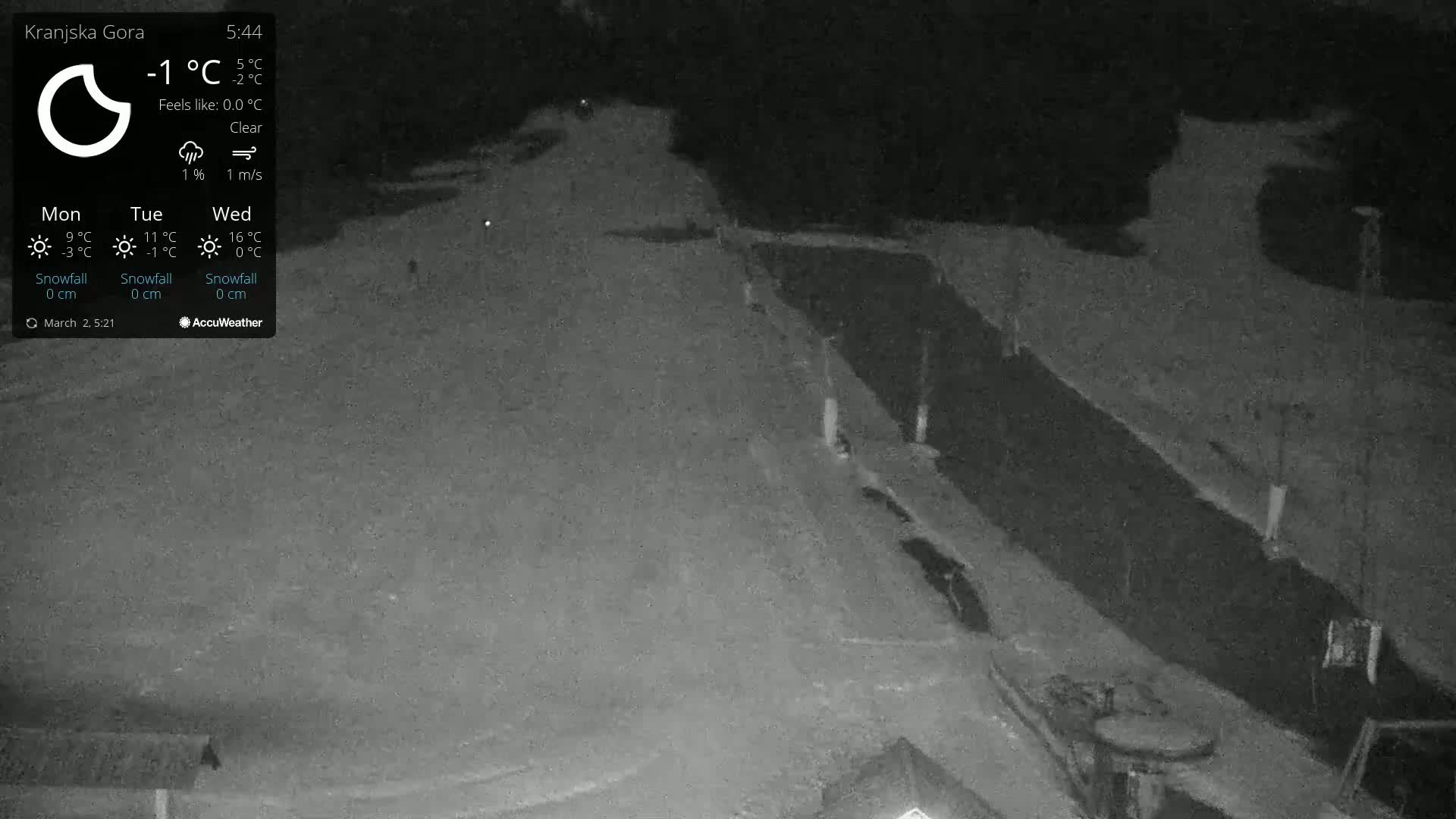 A nighttime, clear, low-light view of a snow-covered, possibly mountainous, area with a road or path visible.