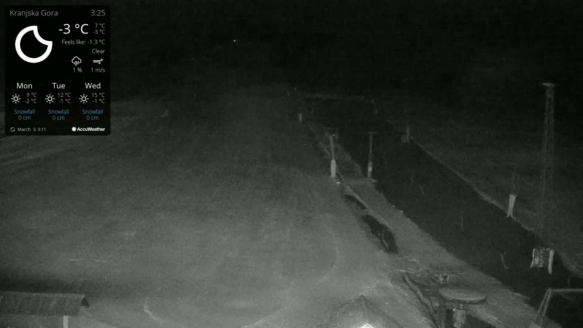 A nighttime, clear view of a snow-covered, dark area with some structures and poles visible.